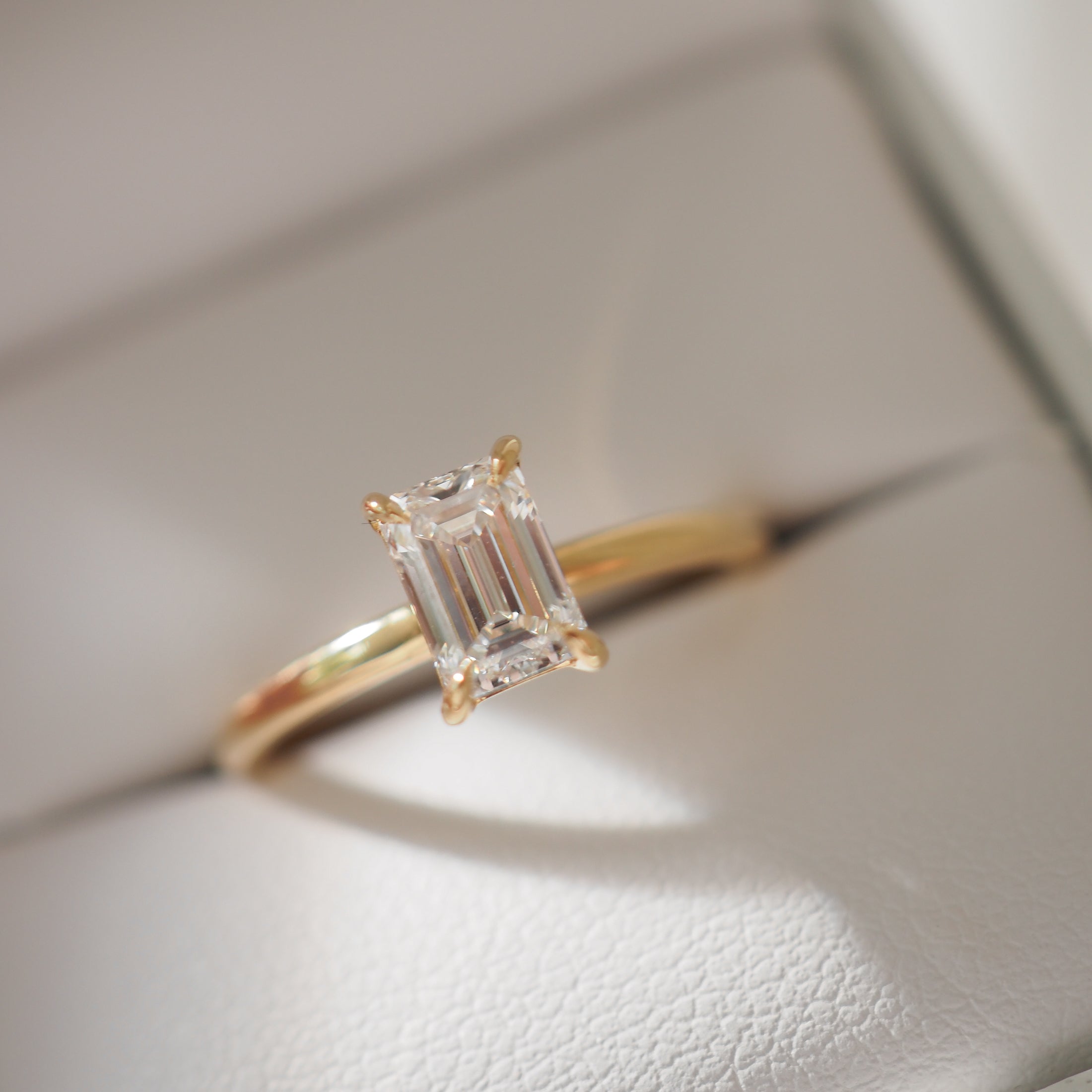 Emerald-cut diamond solitaire ring set on a gold band, displayed in a white jewellery box, showcasing luxury and elegance.