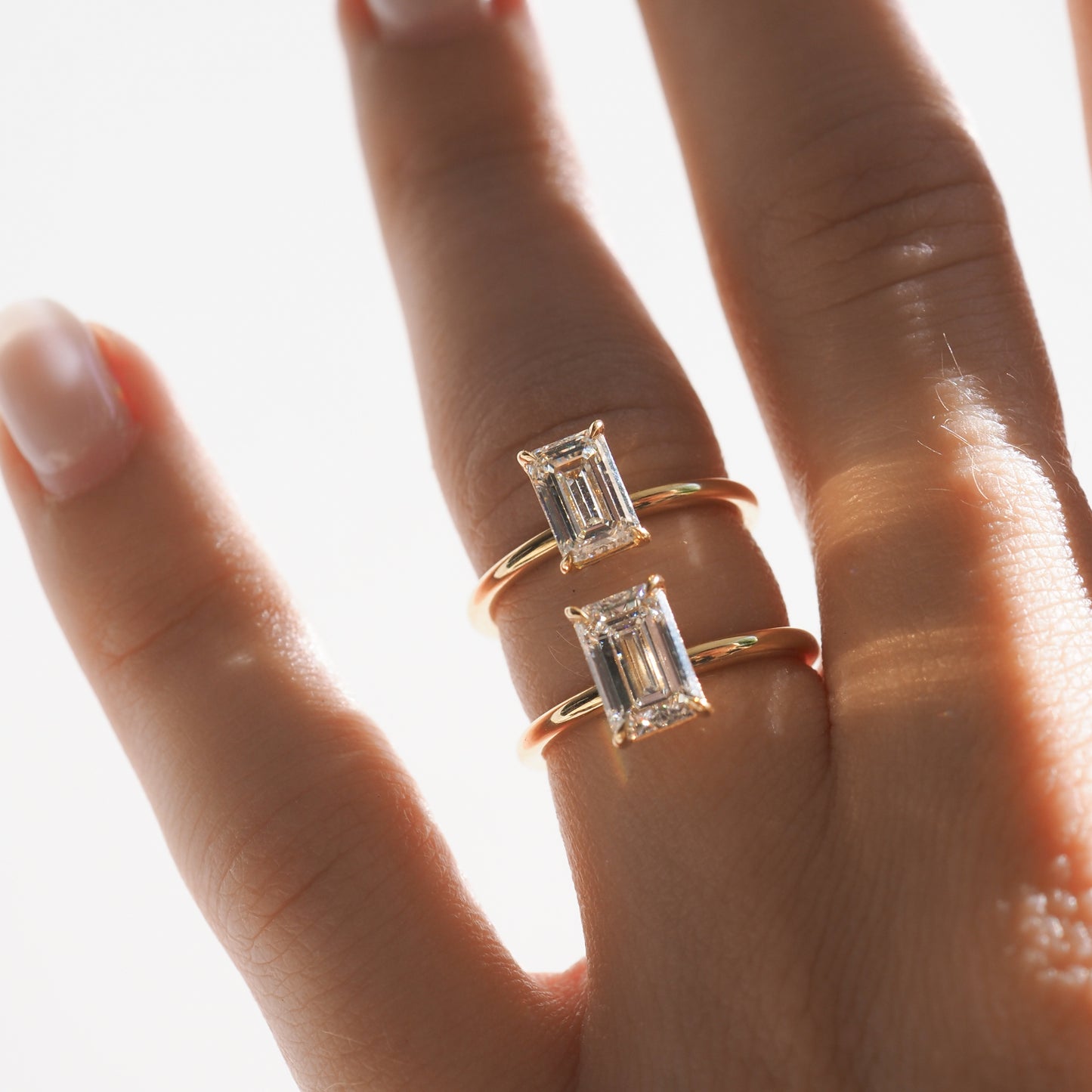 Two gold rings with rectangular diamond settings adorn adjacent fingers, glistening in soft lighting, highlighting luxury and elegance.