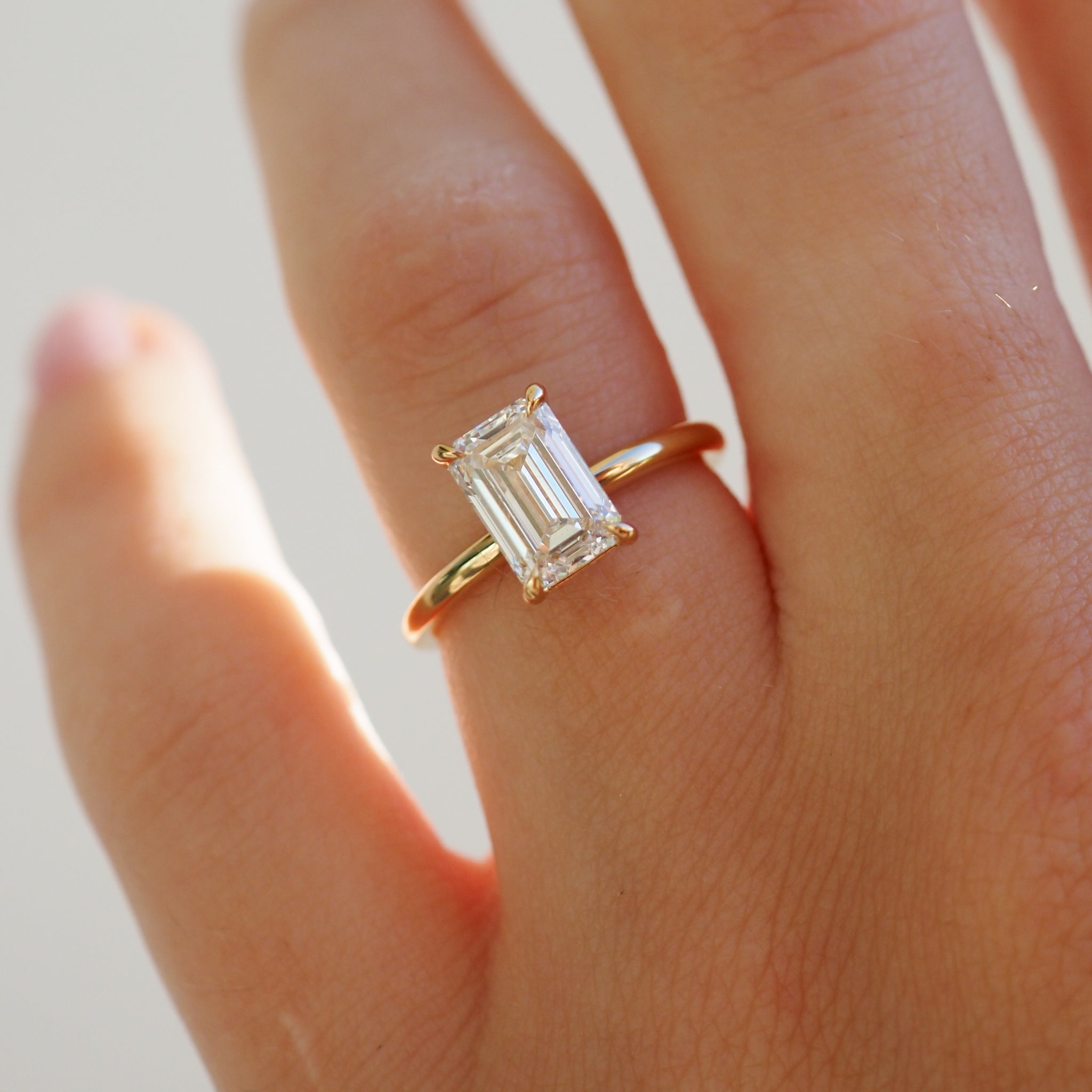 Gold ring with an emerald-cut diamond on a finger, showcasing elegant luxury jewellery design, ideal for high-end fashion and bridal jewellery.