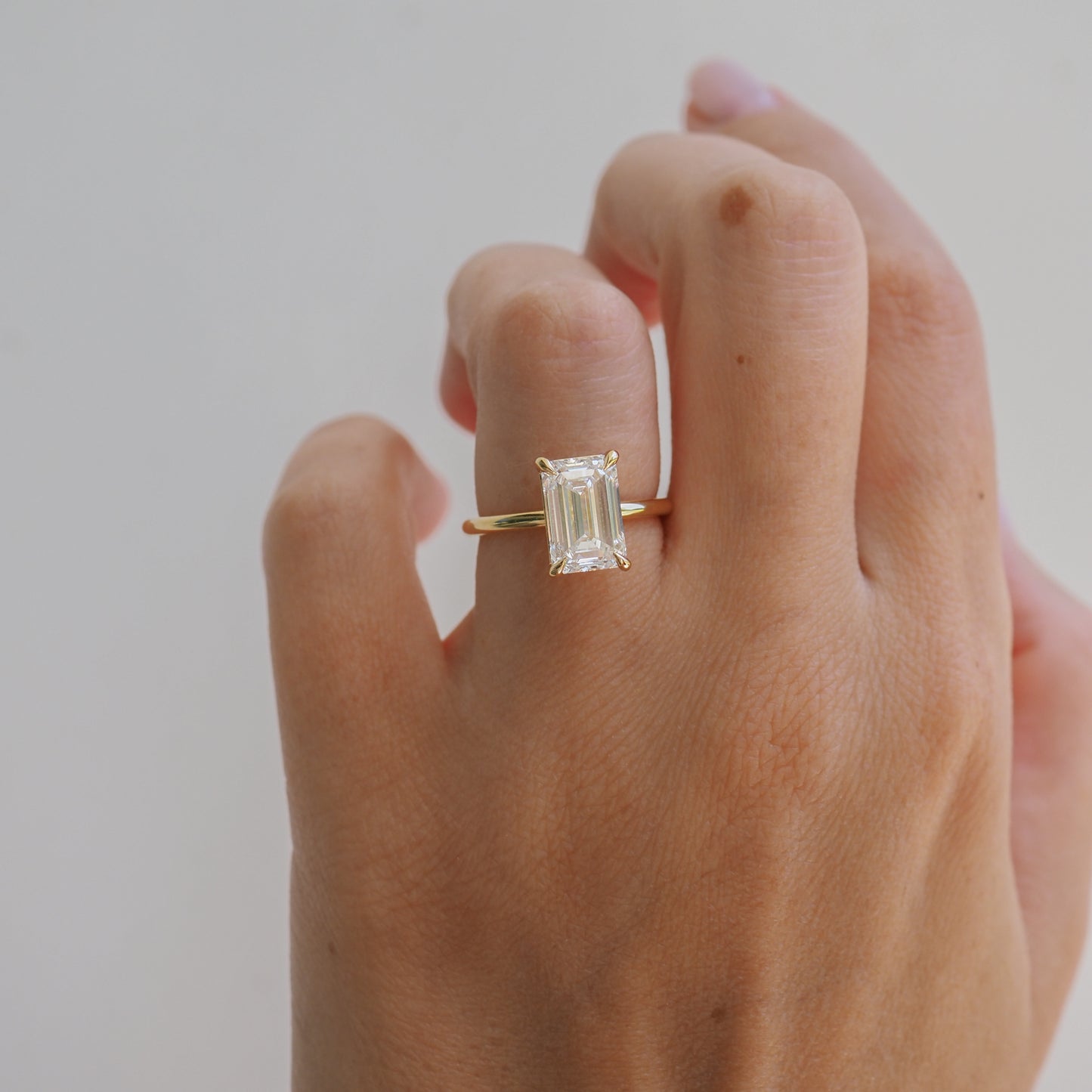 A hand wearing a gold ring with a large, emerald-cut diamond set in a minimalist band, symbolising luxury and elegance.