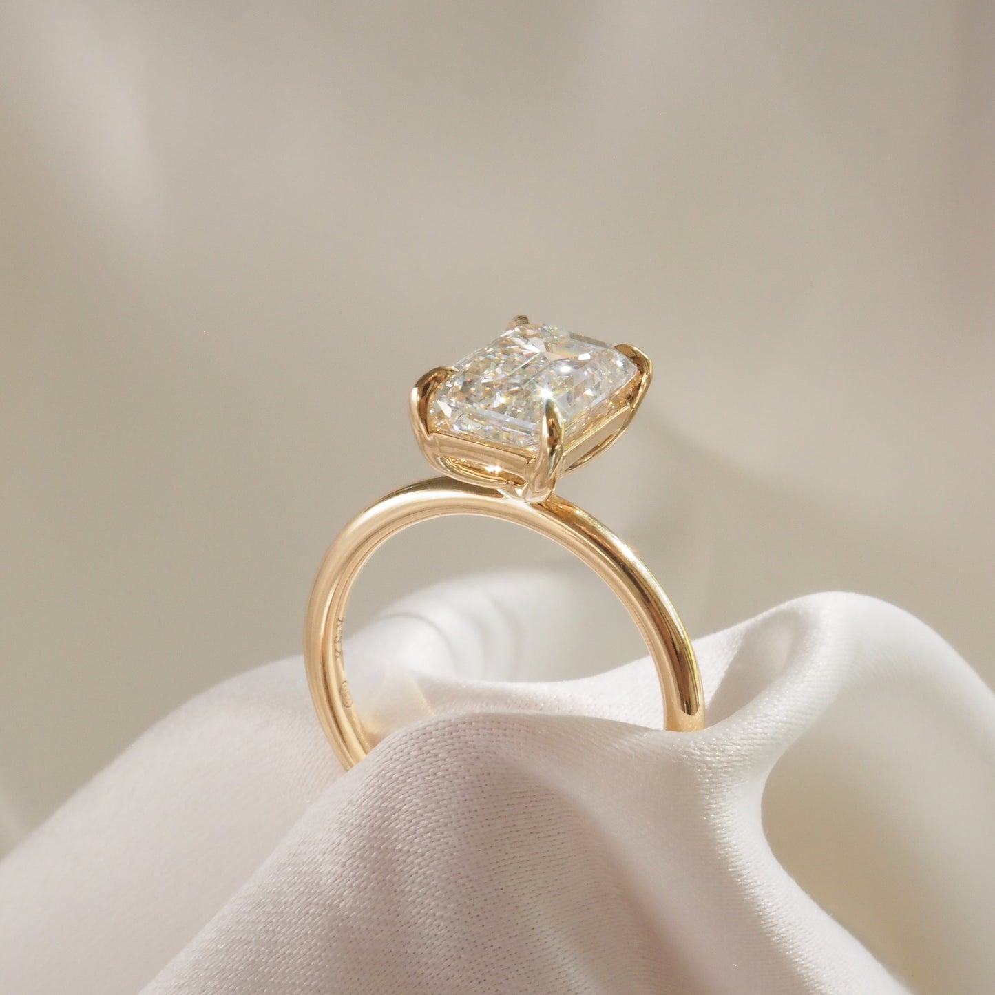 Elegant gold ring featuring a radiant-cut diamond, elegantly displayed on soft white fabric, showcasing luxury jewellery craftsmanship.