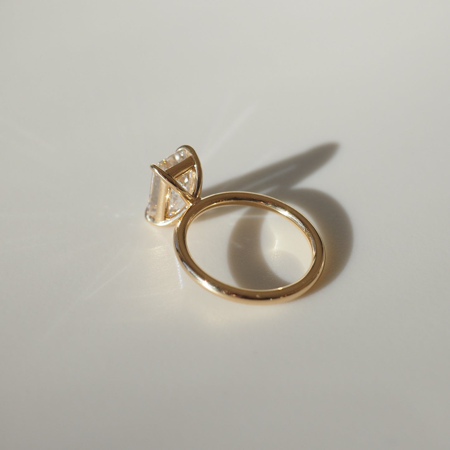 Elegant gold ring with a prominent gemstone set in a unique, modern prong design, casting a soft shadow on a smooth surface. Perfect for luxury jewellery lovers.