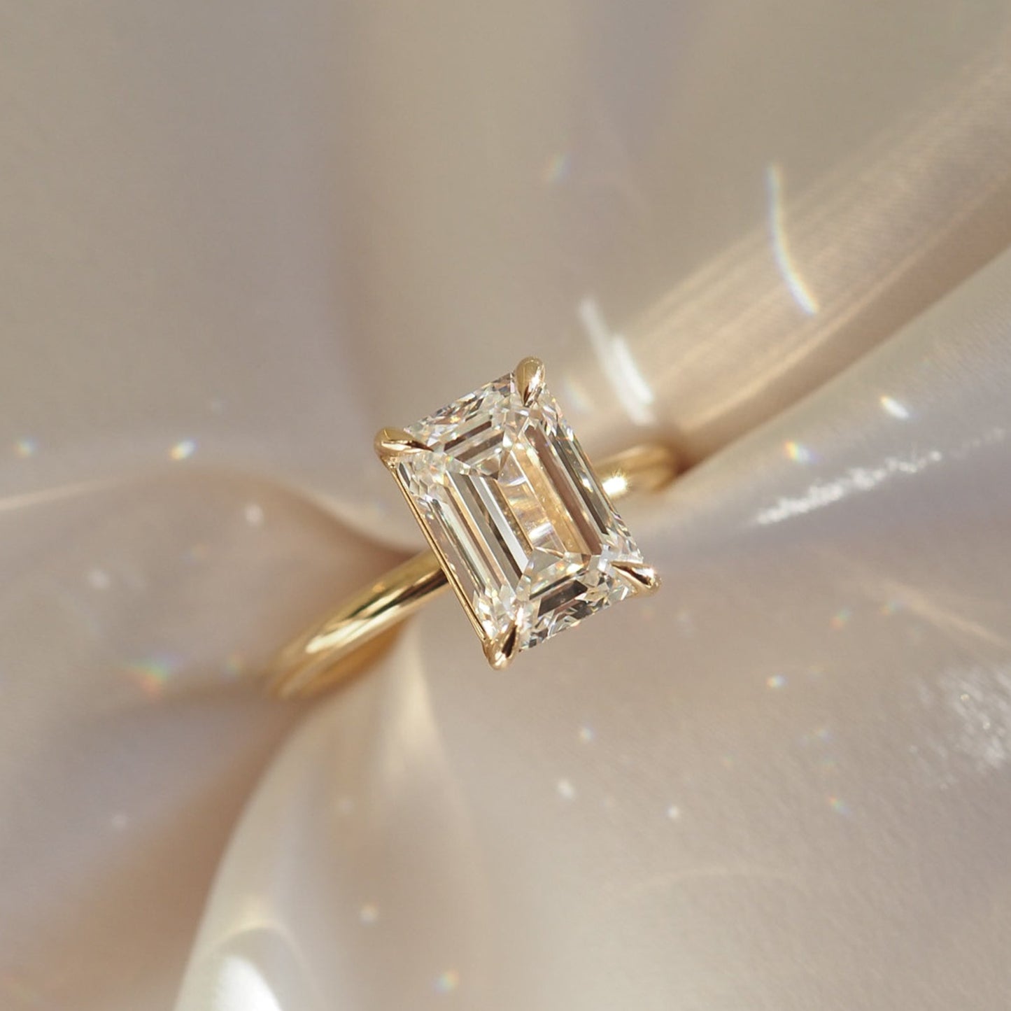 Emerald cut diamond ring with a gold band on a soft, shimmering fabric background. Luxurious, elegant jewellery design.