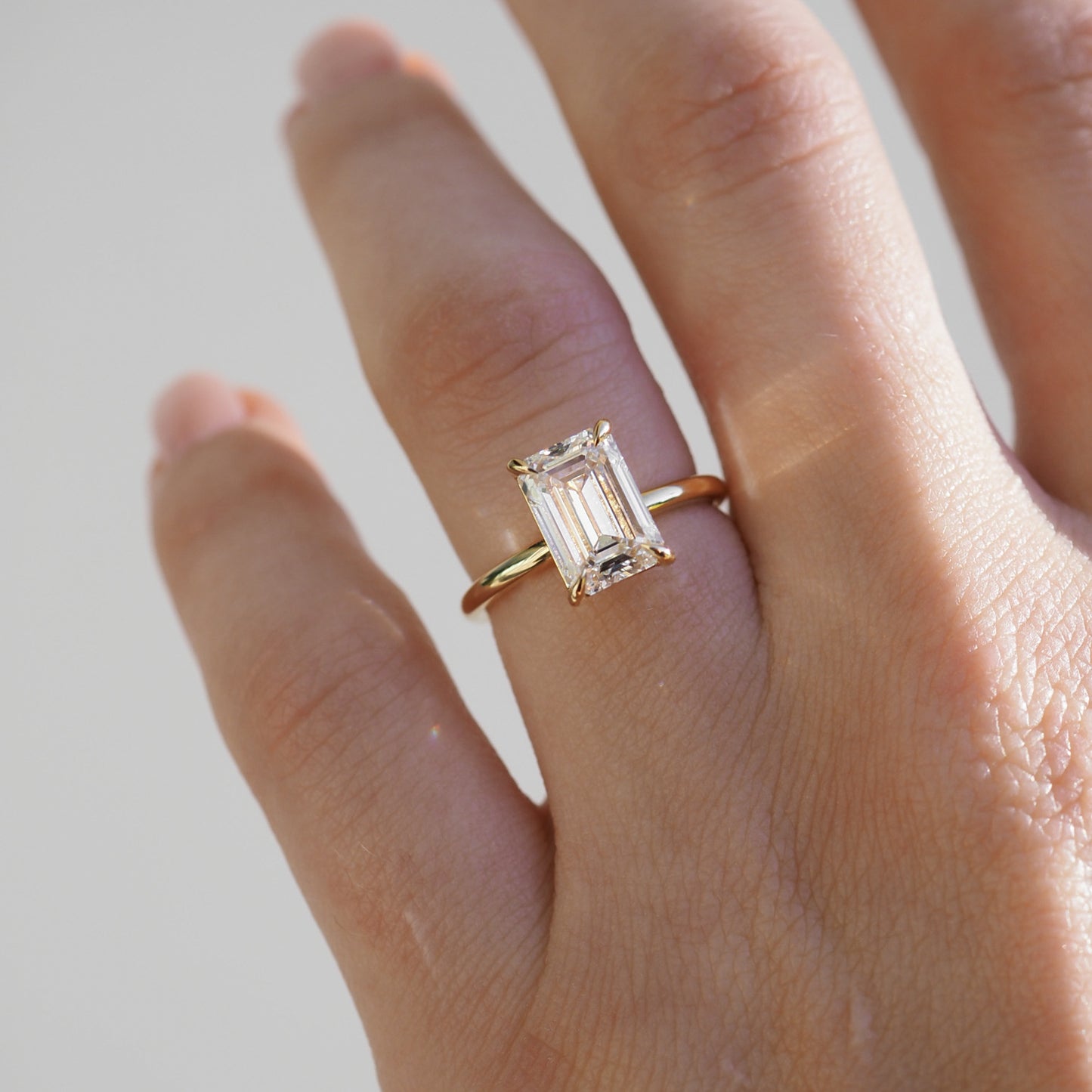Hand wearing an emerald-cut diamond ring on a gold band, catching light. Luxurious and elegant jewellery showcasing refined craftsmanship.