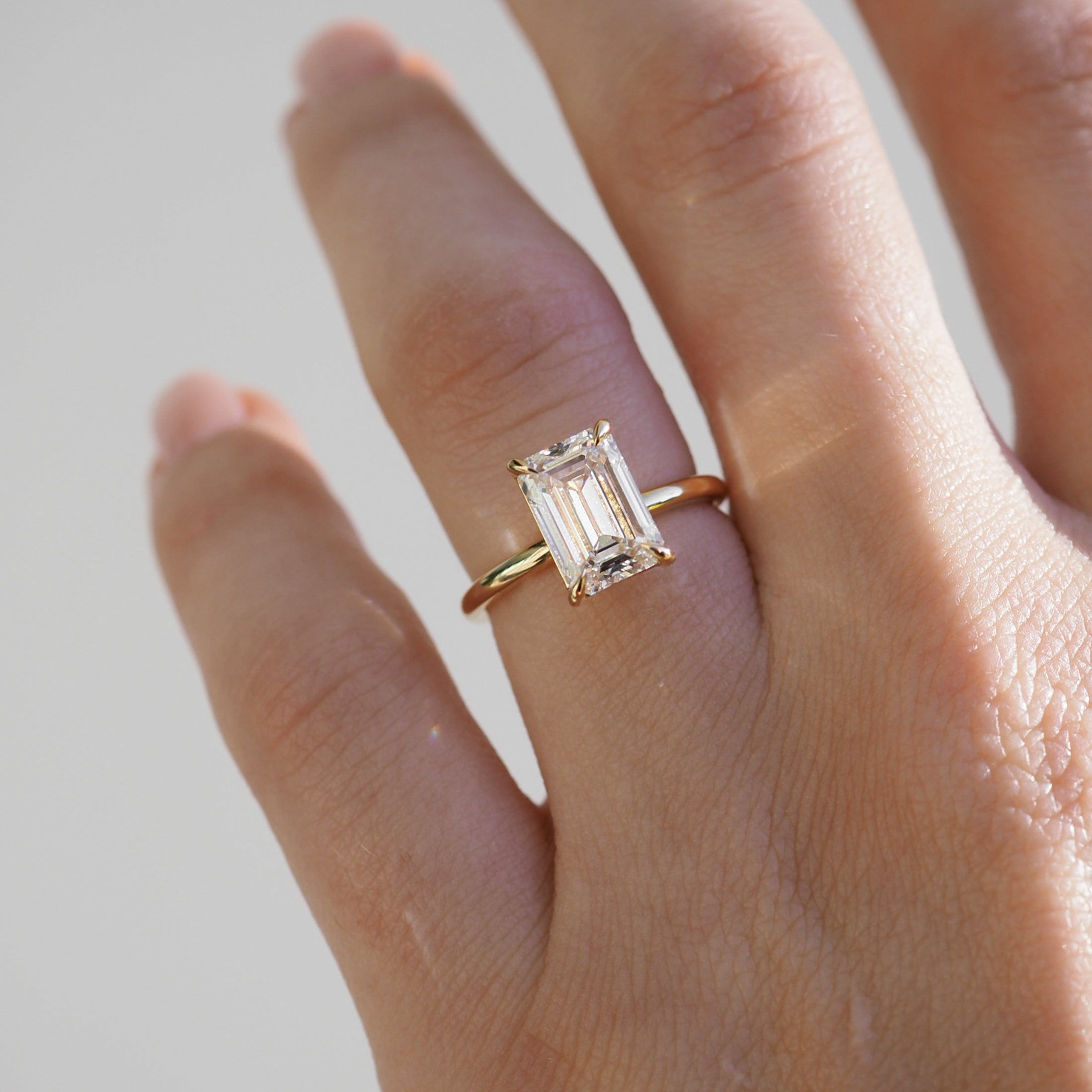Hand wearing an emerald-cut diamond ring on a gold band, catching light. Luxurious and elegant jewellery showcasing refined craftsmanship.