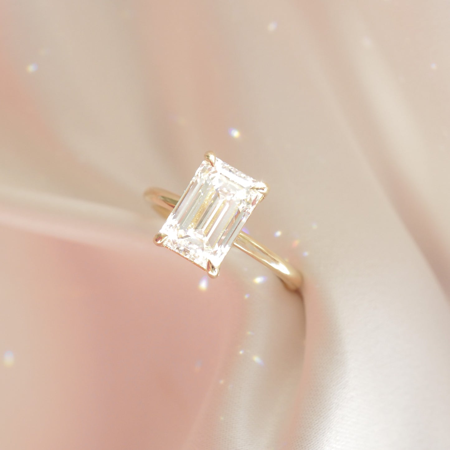 Emerald cut diamond ring with a gold band on a soft, shimmering fabric background. Luxurious, elegant jewellery design.