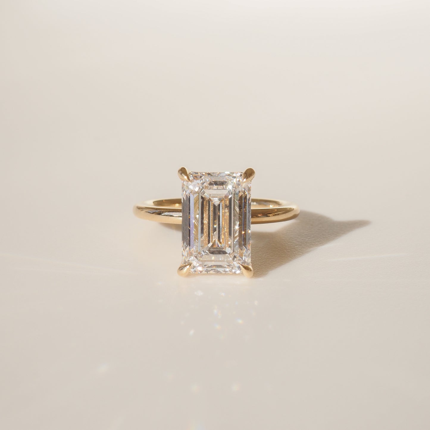 Emerald-cut diamond ring with a gold band, elegantly displayed on a soft beige background, exuding luxury and sophistication.