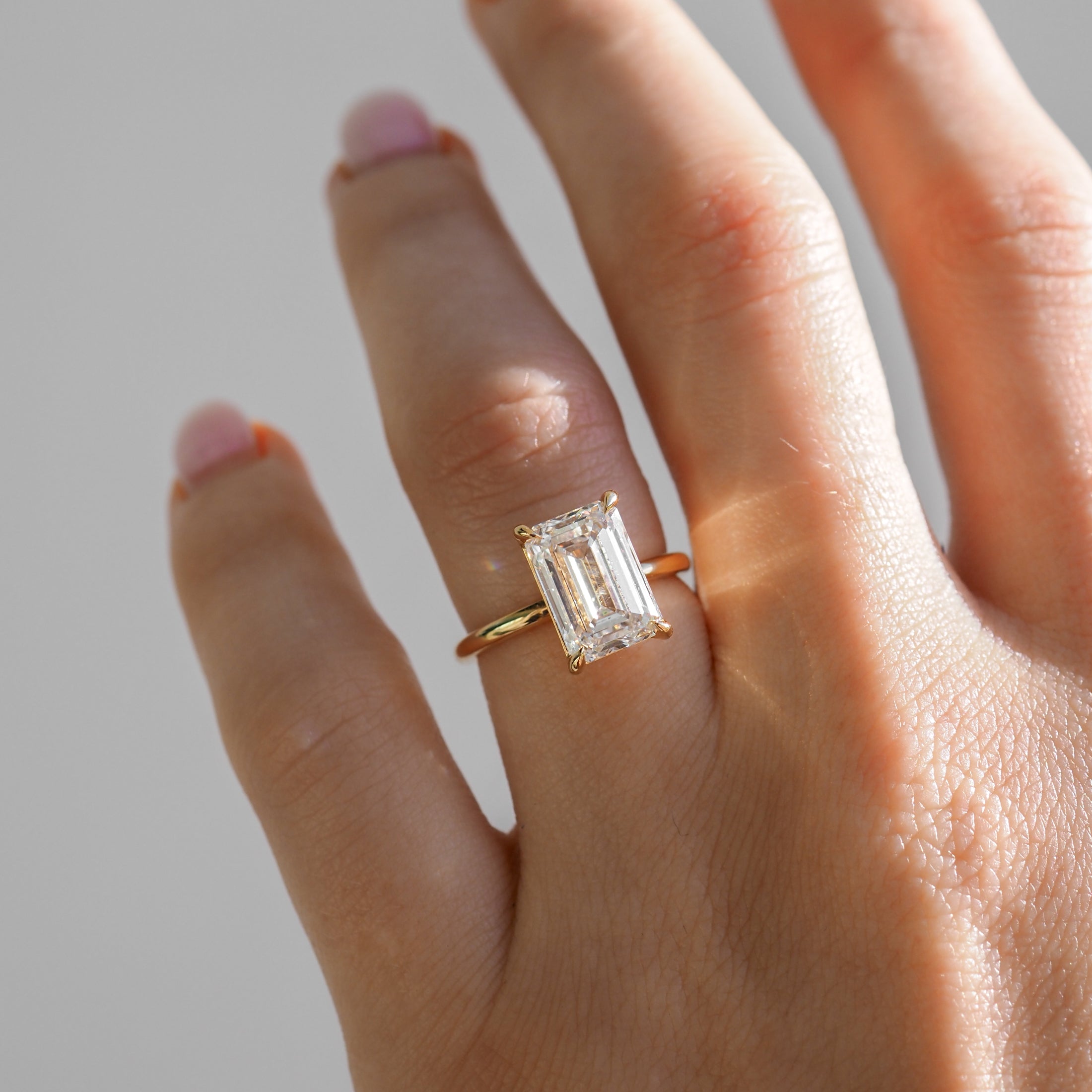 Emerald cut diamond ring on a hand, gold band reflecting soft light. Perfect for luxury jewellery lovers.