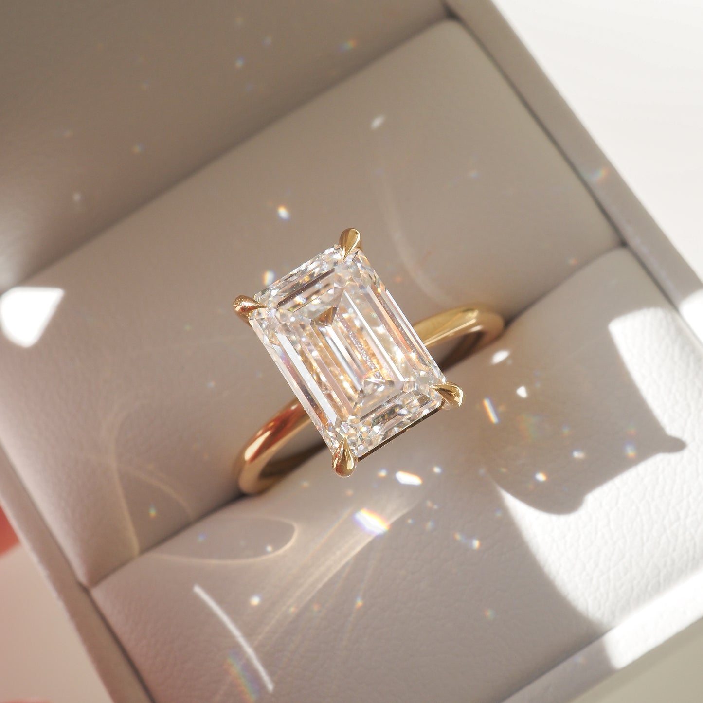 Emerald-cut diamond ring with gold band in a white jewellery box, capturing light reflections. Ideal luxury engagement piece.