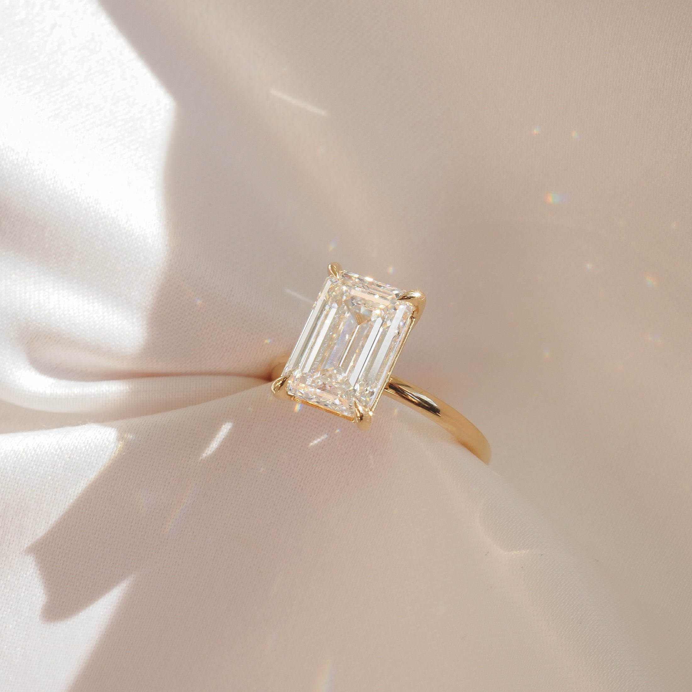Emerald-cut diamond ring with gold band on soft beige fabric, sparkling under gentle light. Luxurious high-end jewellery.