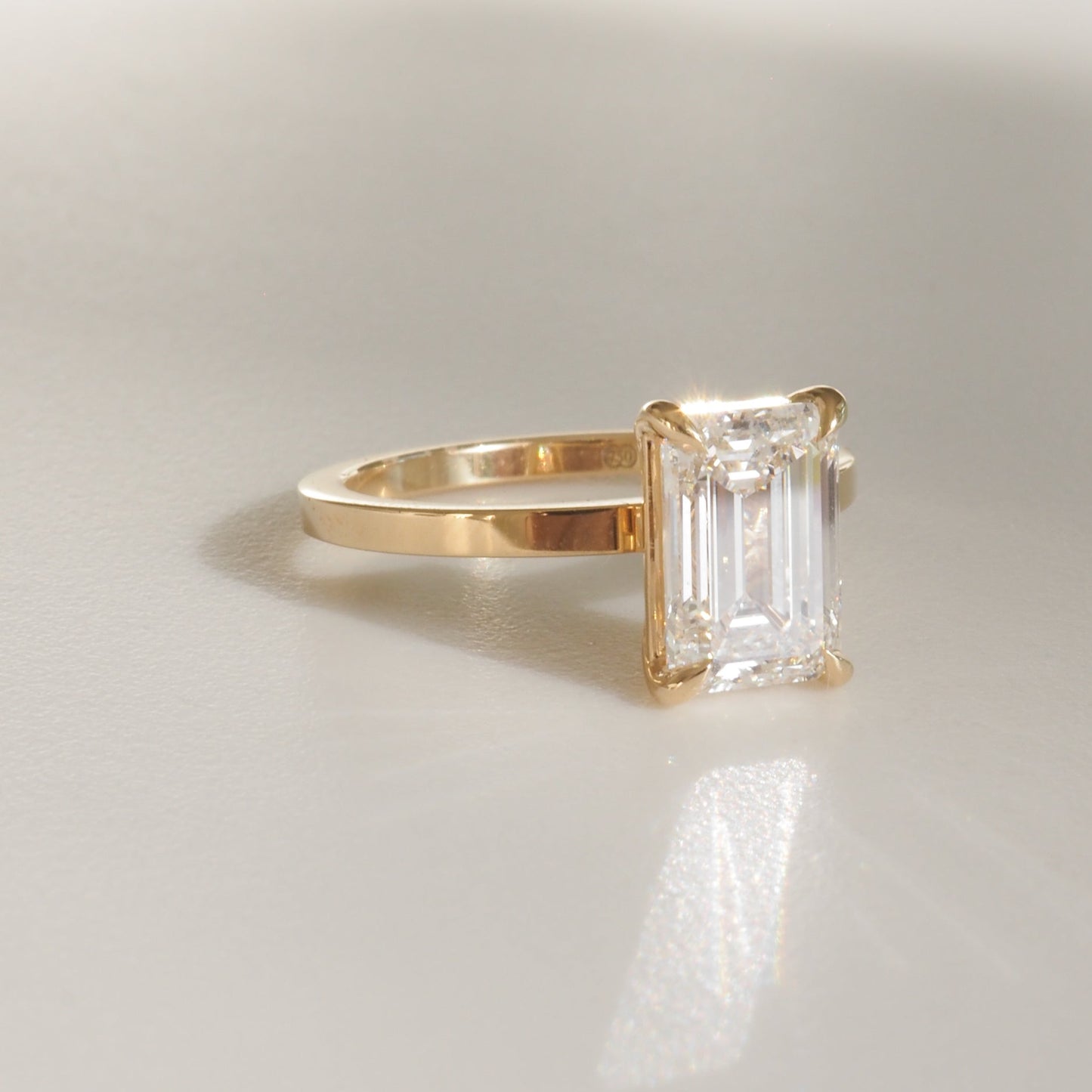 Gold ring with a large emerald-cut diamond on a light background. The luxurious jewellery piece showcases minimalist elegance.