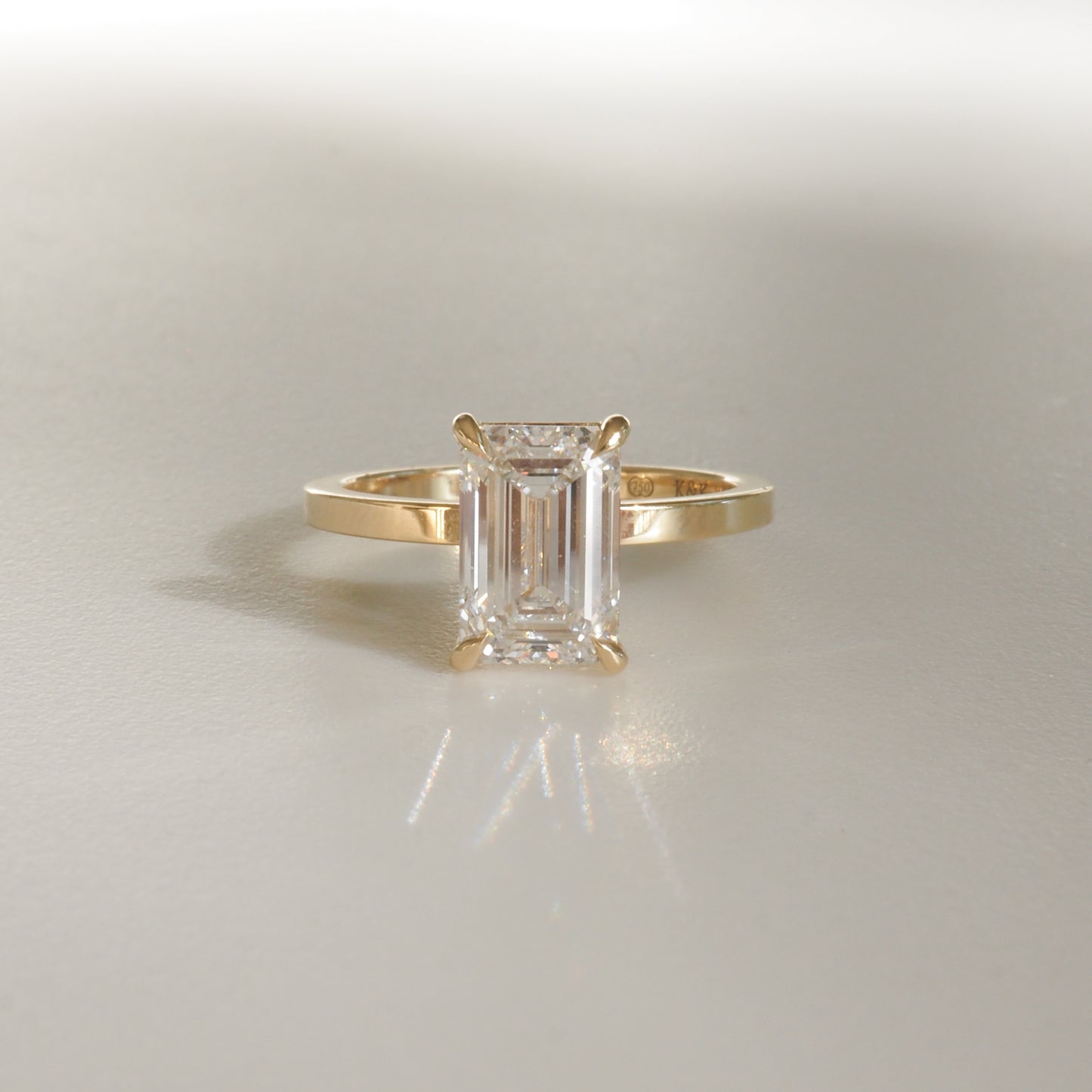 Emerald-cut diamond ring with gold band, reflecting light on a soft background; elegant luxury jewellery piece.