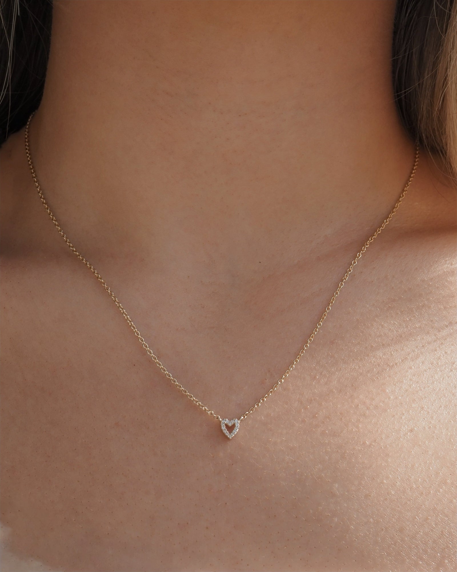 A delicate gold chain necklace with a small heart-shaped pendant featuring hand set lab grown diamonds, shown worn on a model's neck.