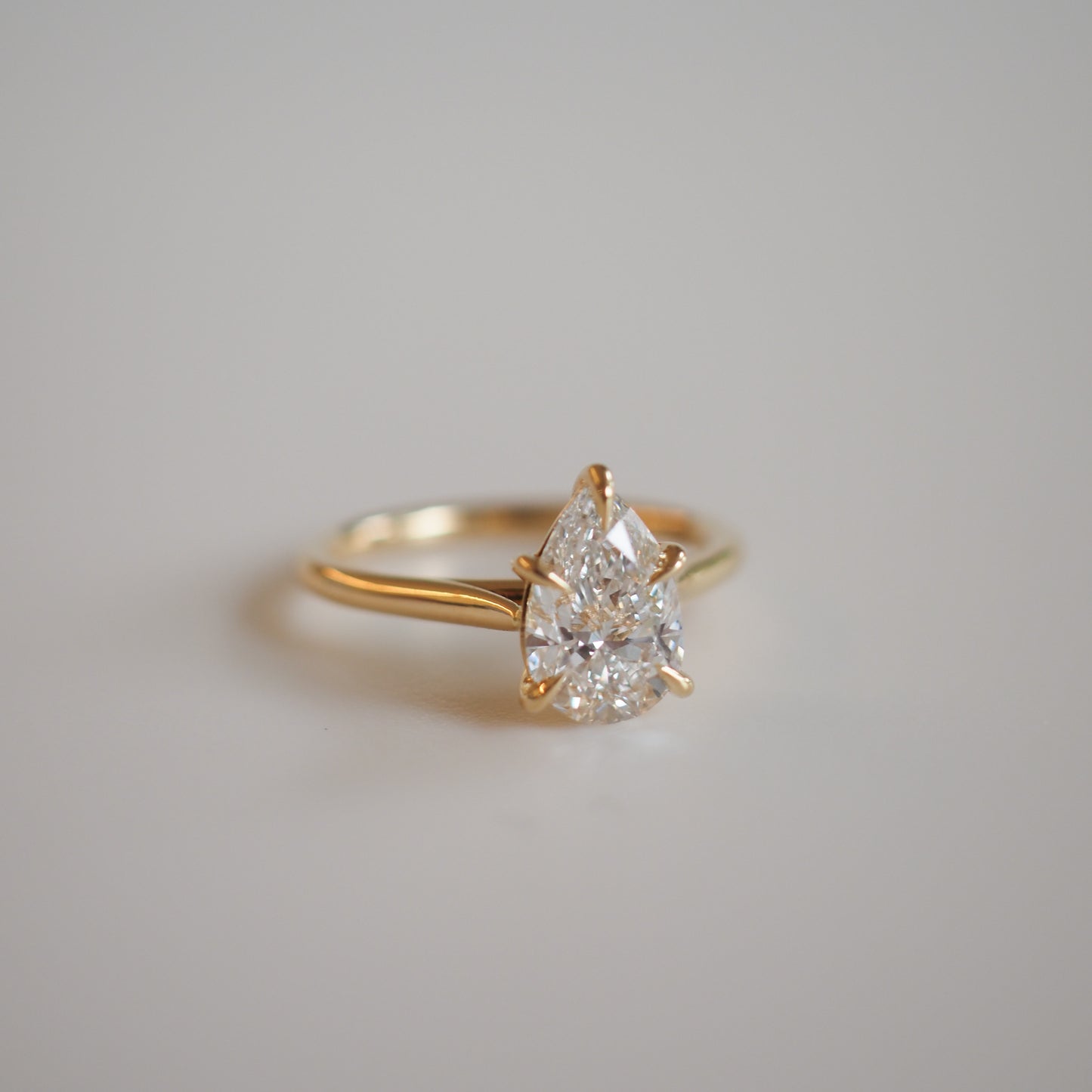 Gold ring with a pear-shaped diamond solitaire in a prong setting on a smooth surface. Luxurious and elegant jewellery piece.