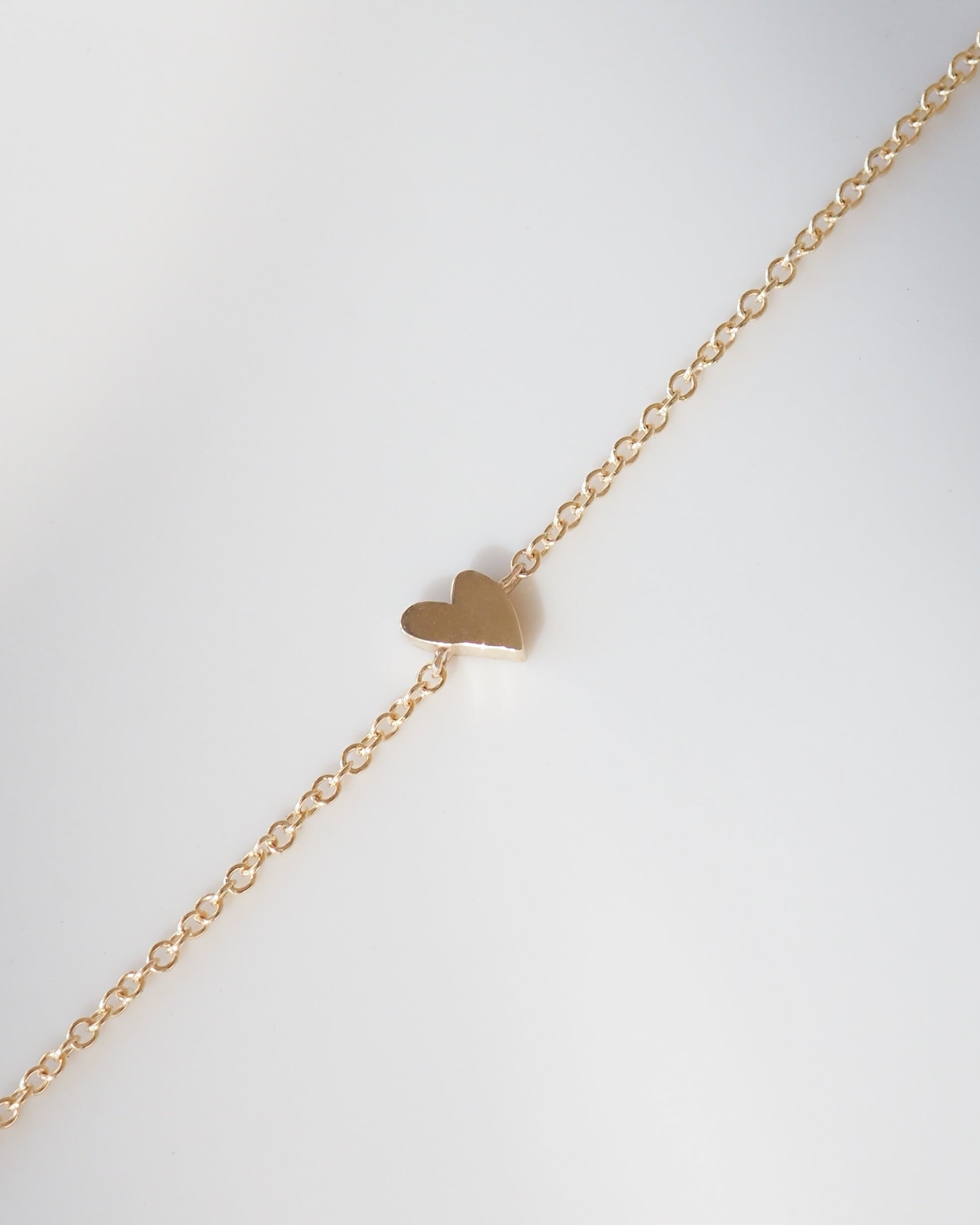 Gold heart-shaped pendant on a gold chain against a light gray background