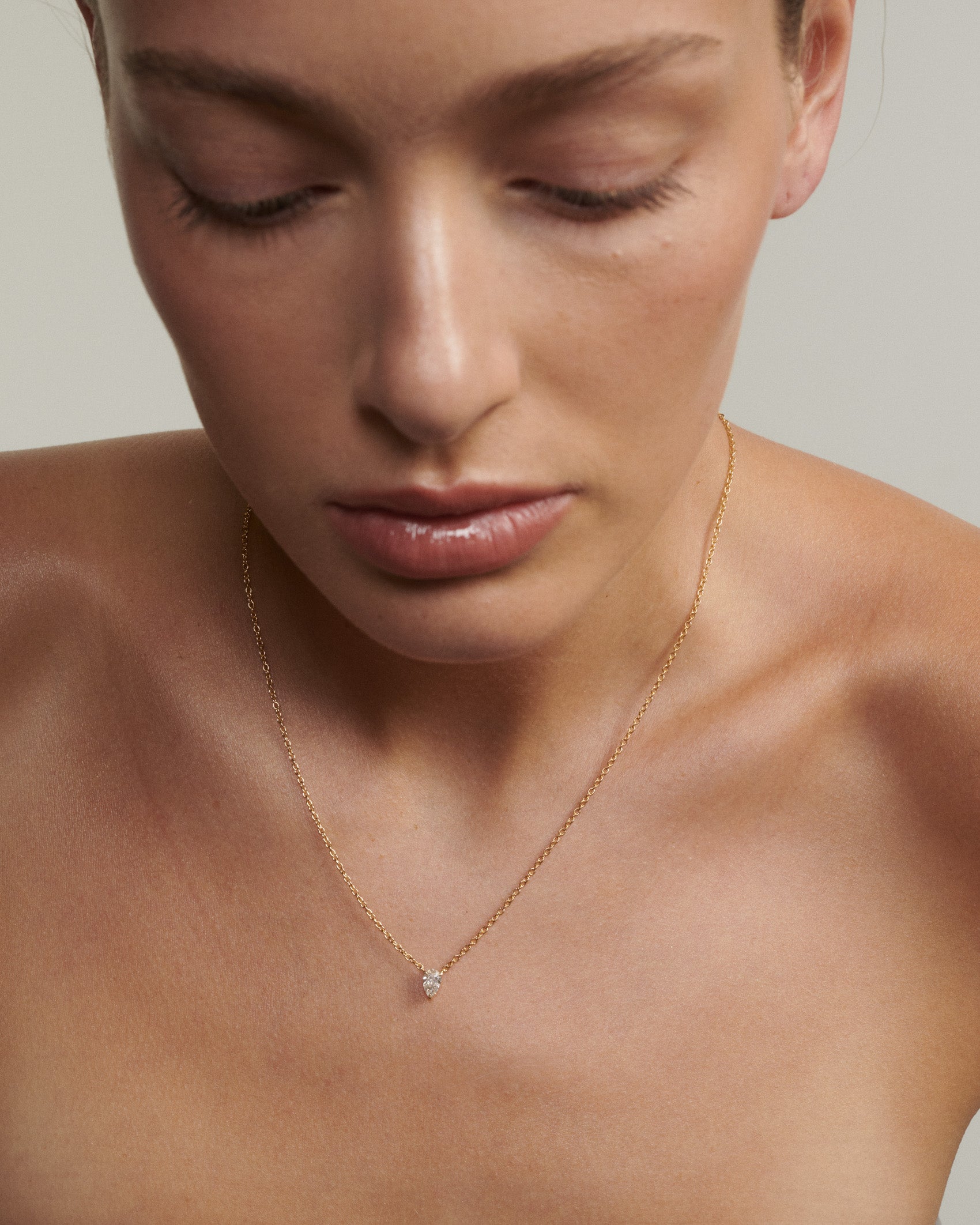 Close-up of a person wearing a delicate necklace with a small diamond pendant. [text overlay: Andrea wears the 0.5ct Pear Diamond Necklace]