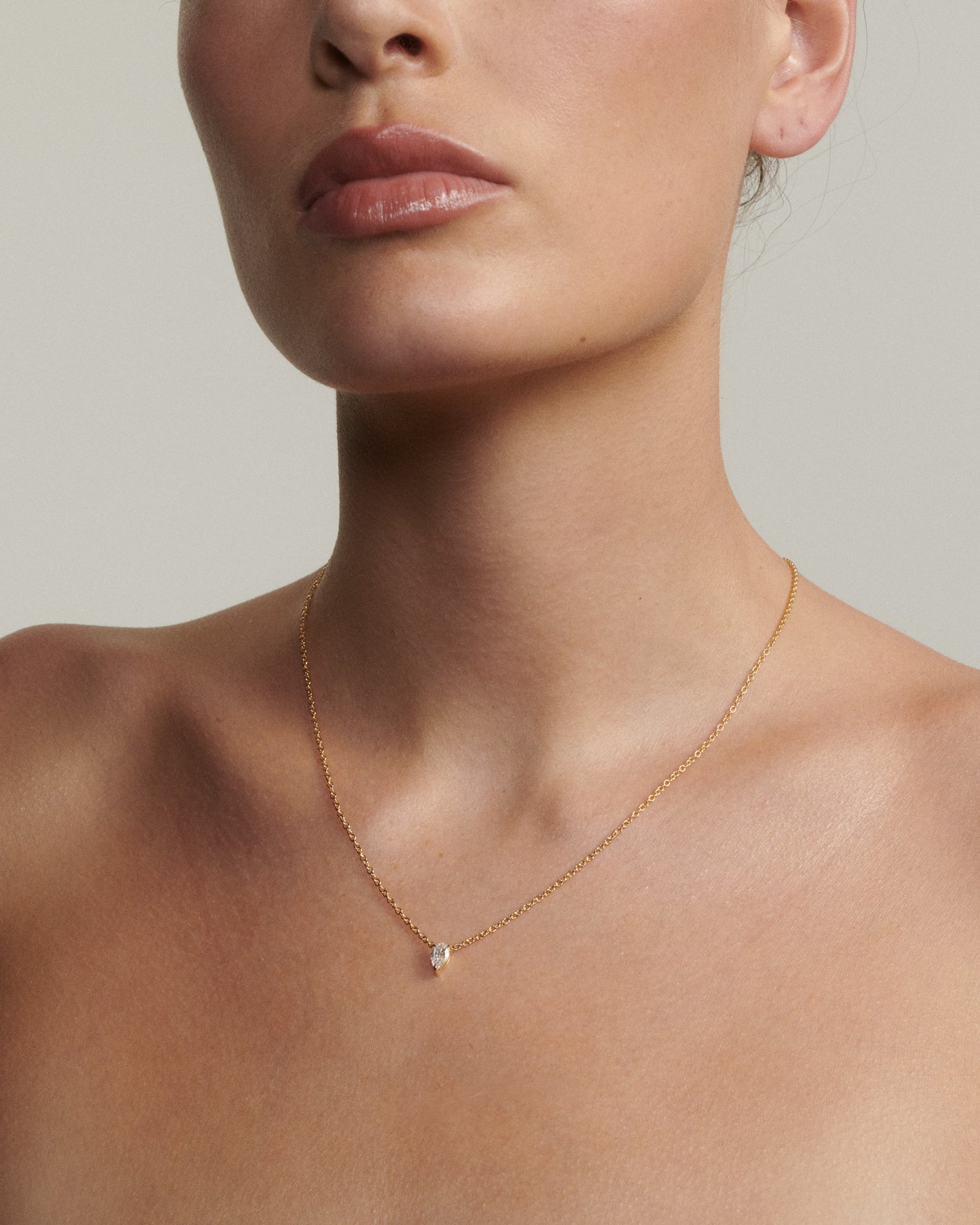 Close-up of a person wearing a delicate gold necklace with a small pendant on a neutral background