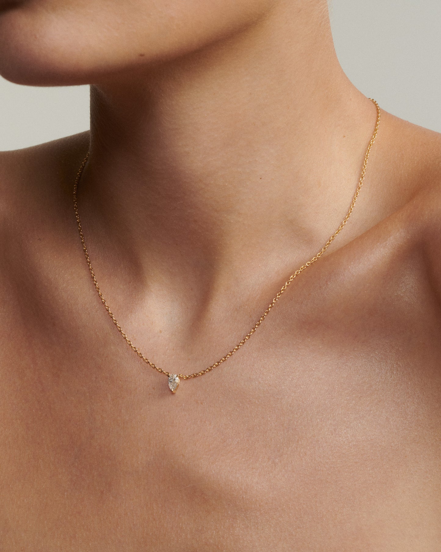 Gold necklace with a small pendant on a person's neck against a neutral background