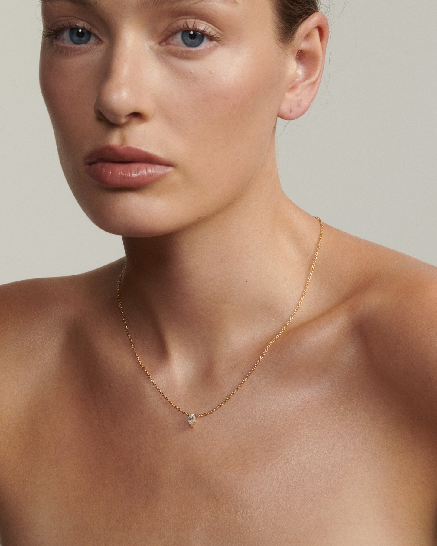 Woman wearing a delicate gold necklace with a small pendant against a neutral background
