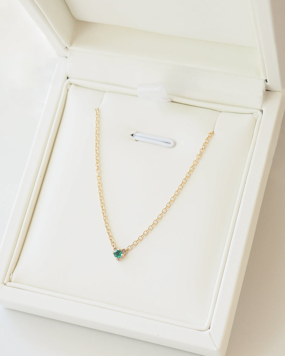 Gold necklace with a green gemstone in a white jewelry box