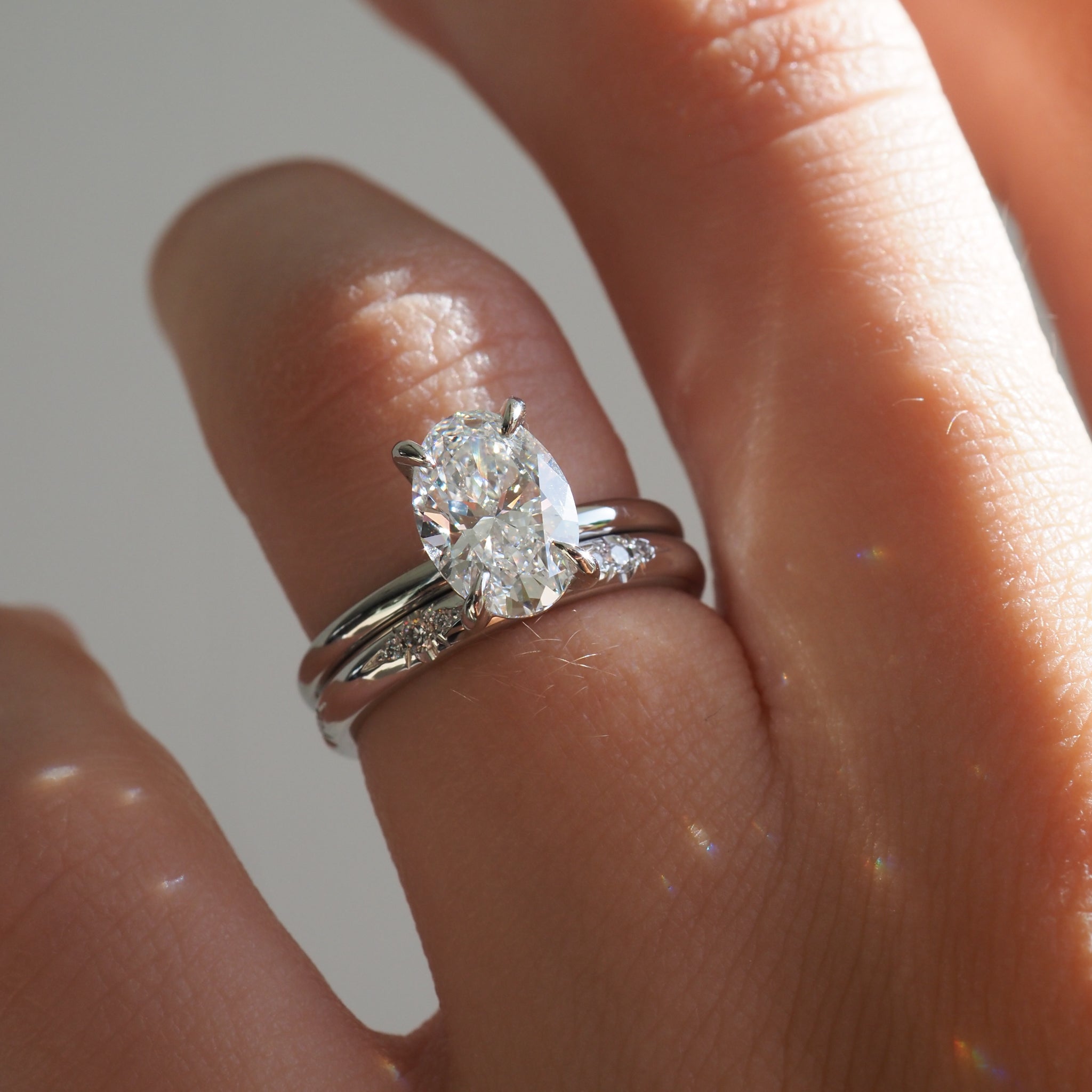 Close-up of a hand adorned with an elegant double-banded engagement ring featuring a large oval diamond, shining with subtle light reflections.