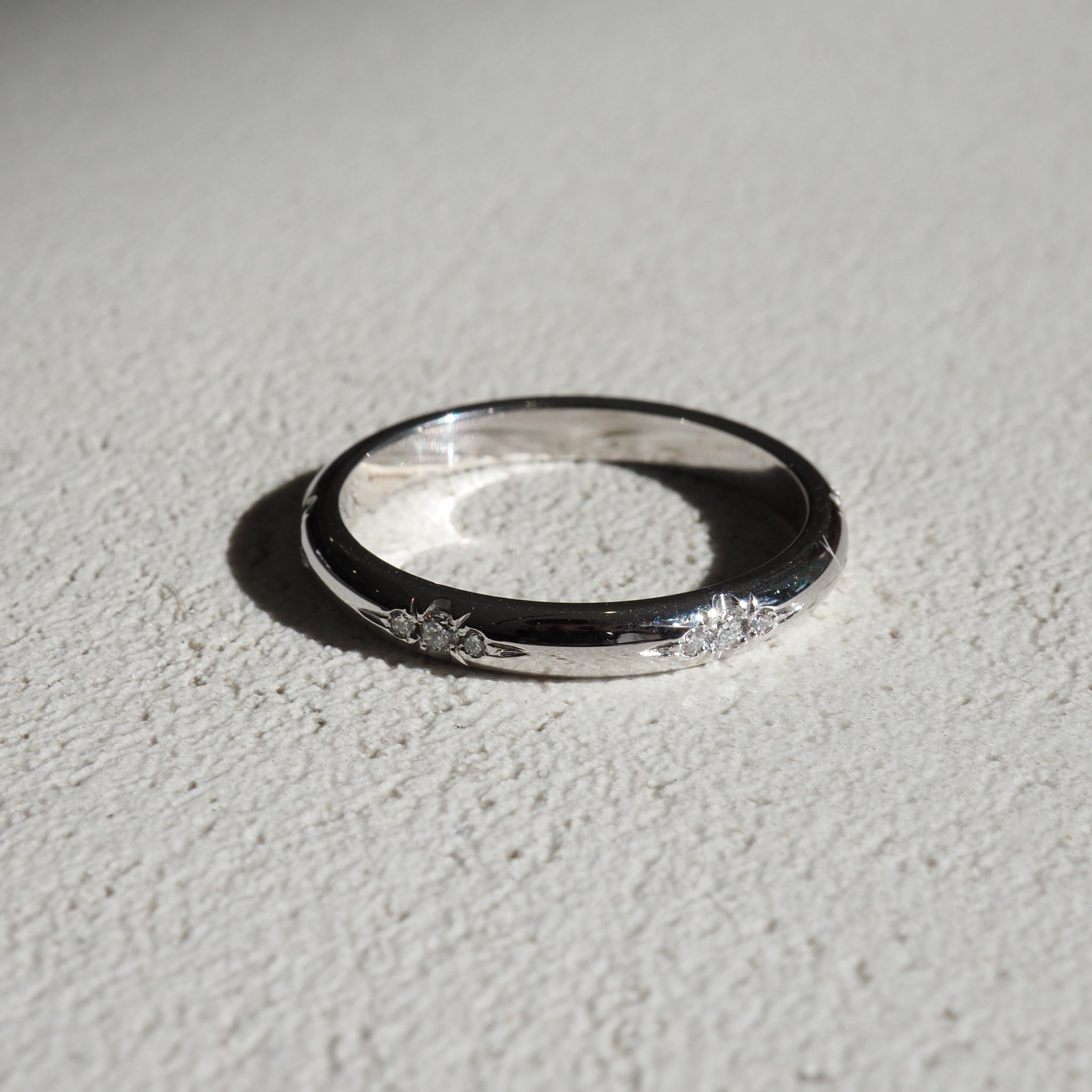 Elegant silver ring with floral engravings, casting soft shadows on a textured white surface. Ideal for luxe jewellery enthusiasts.