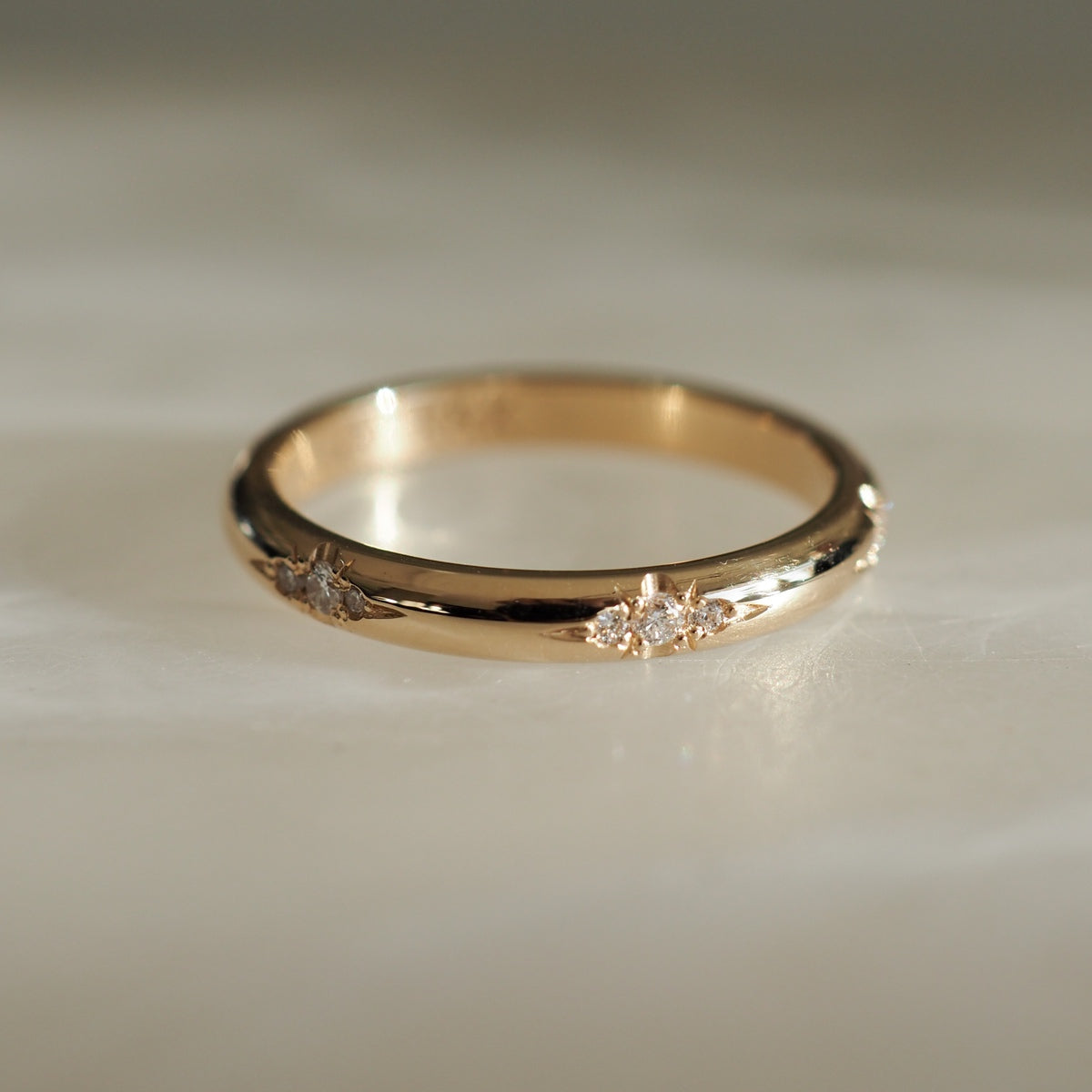 Gold band ring with small diamond accents on a light surface, showcasing luxury jewellery craftsmanship. Ideal for elegant, minimalist style.