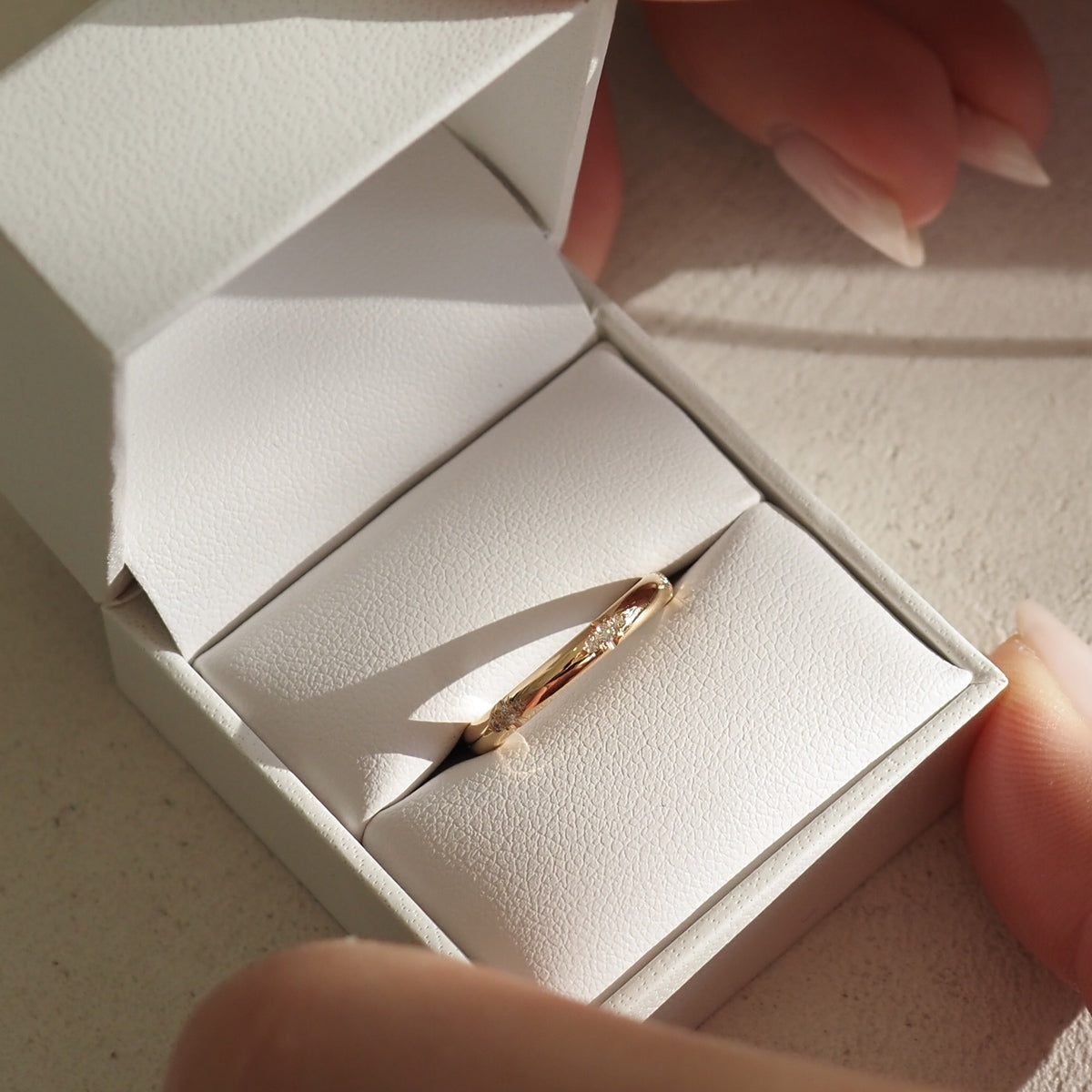 Gold ring with a textured surface displayed in an open white jewellery box, resting on a textured surface with light casting soft shadows.