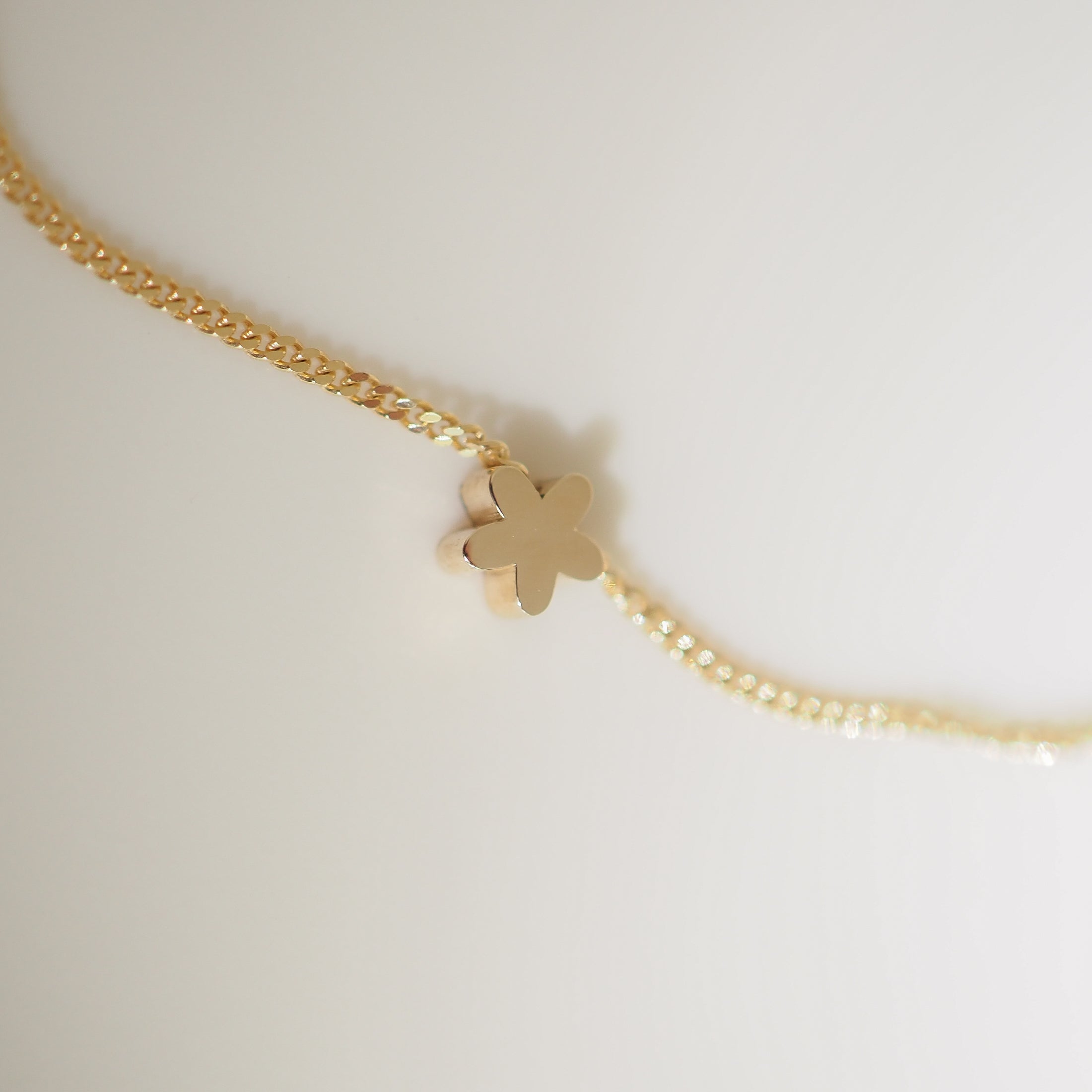 Gold necklace with a delicate flower-shaped pendant on a textured chain, set against a soft, neutral background.