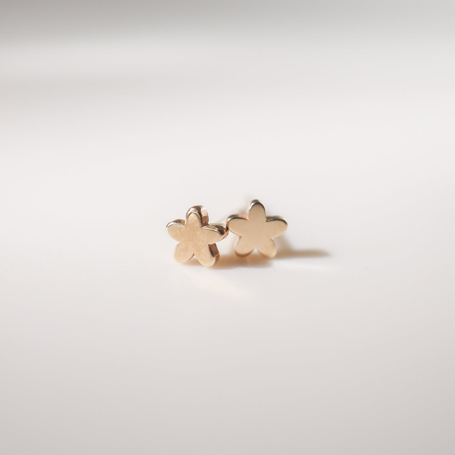 Gold flower-shaped stud earrings on a light background, showcasing luxury jewellery design.