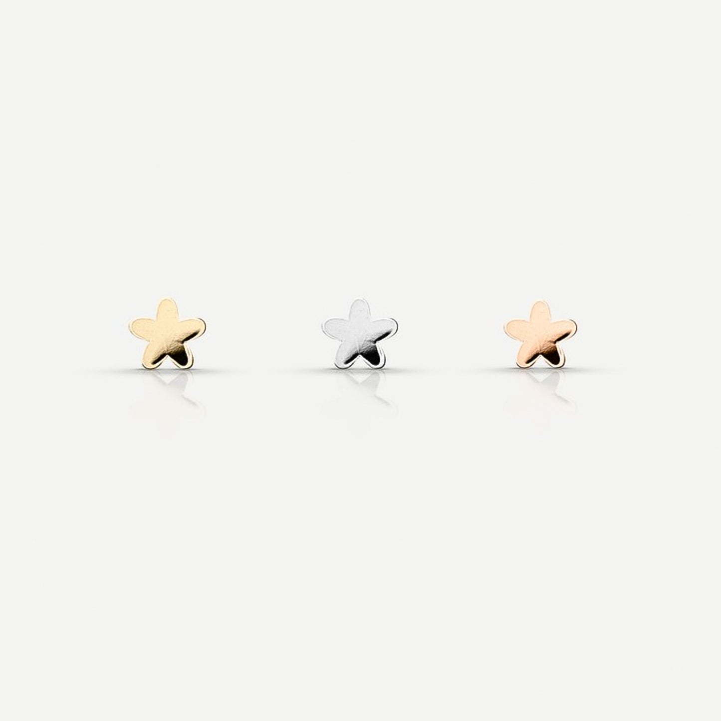 Three star-shaped stud earrings in gold, silver, and rose gold tones are arranged in a row against a light background.