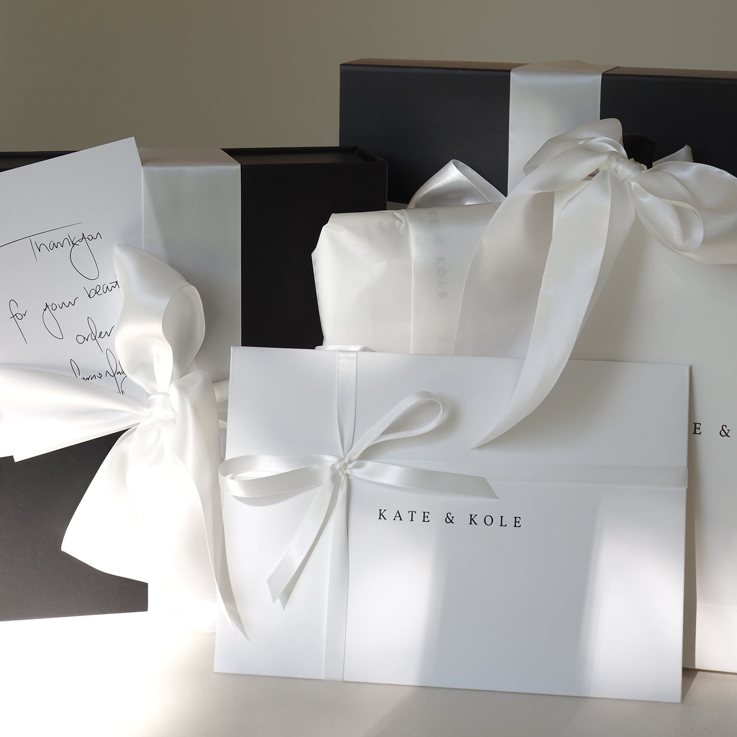 Luxurious Kate & Kole gift boxes elegantly wrapped in white ribbon, featuring a handwritten thank-you note. Perfect for high-end jewellery gifts.