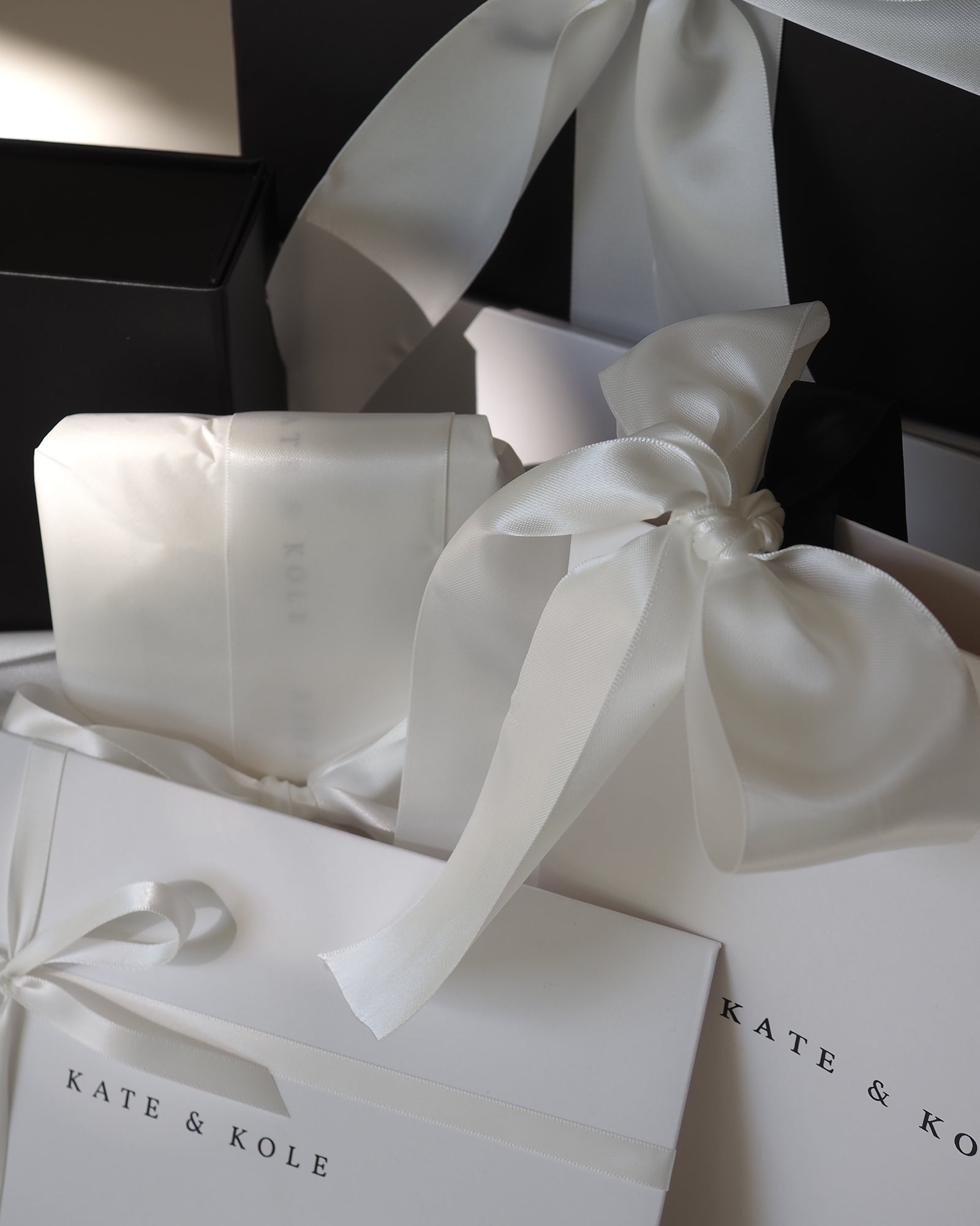 Elegant Kate & Kole packaging featuring white satin ribbons and luxurious black boxes, evoking a high-end jewellery experience.