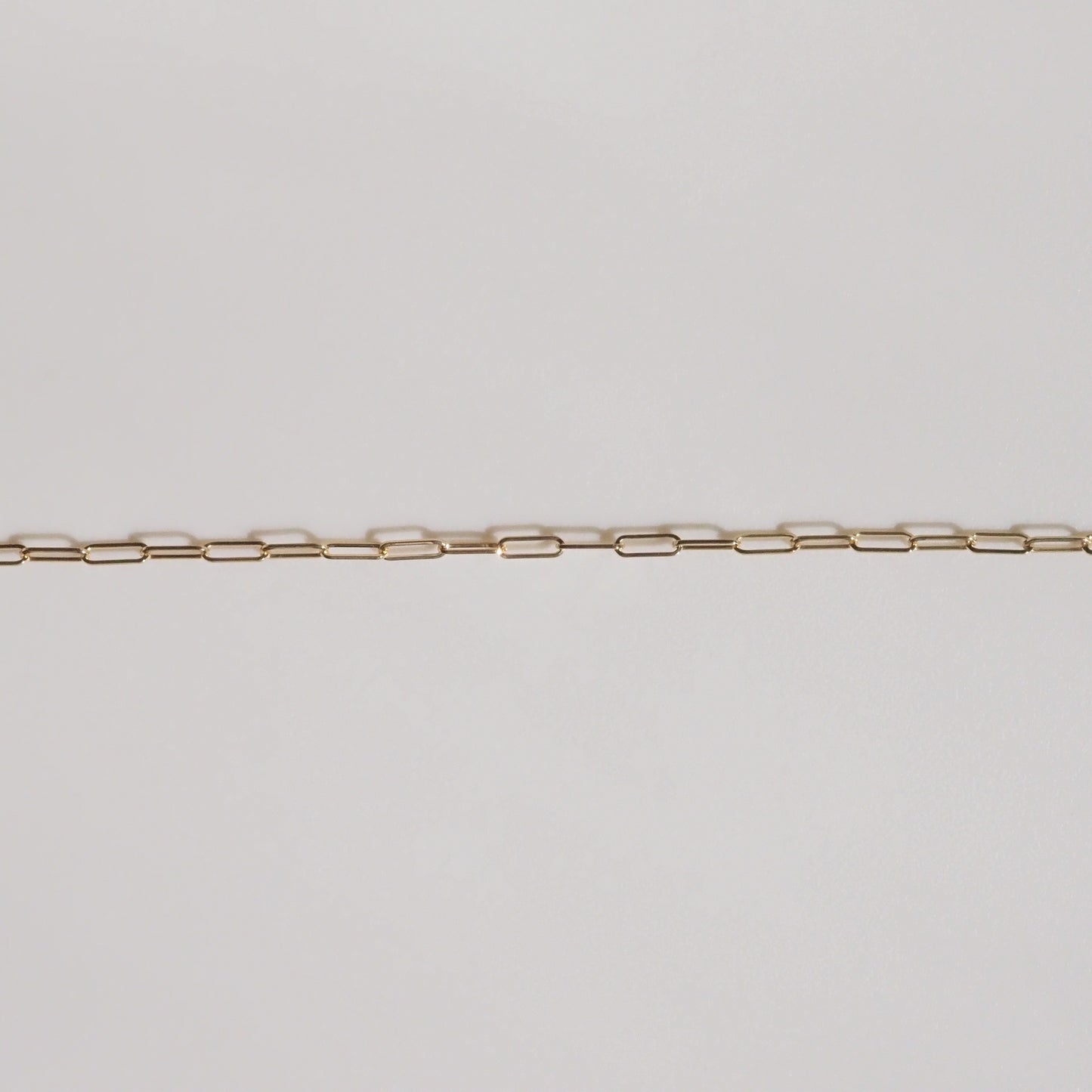 Delicate gold chain with elongated links on a plain background; high-end minimalist jewellery design.