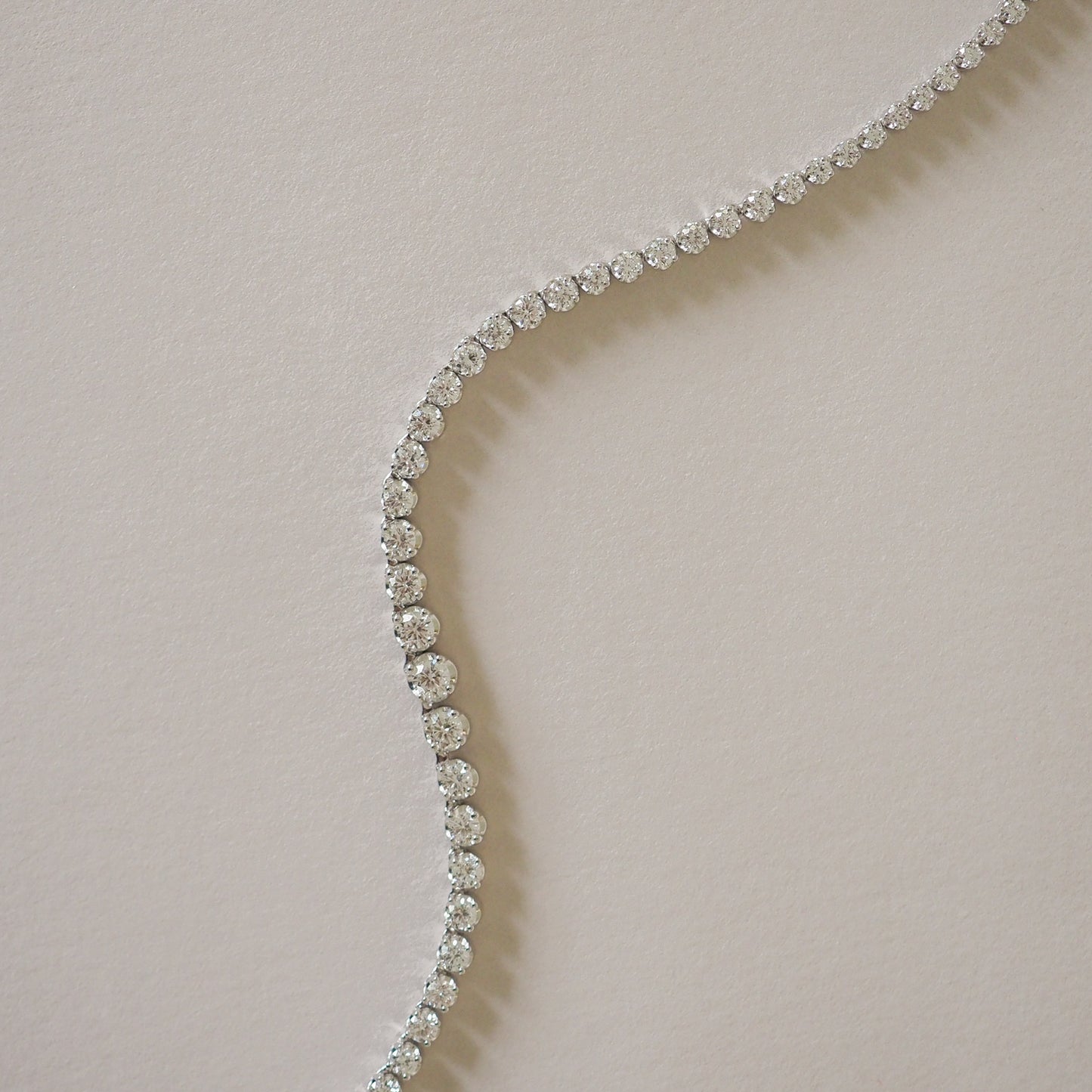 Elegant diamond tennis bracelet curved on a light background, showcasing luxury jewellery design in a high-end, sophisticated style.