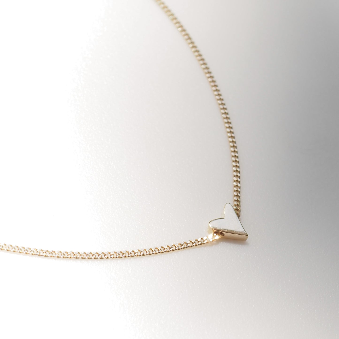 Gold necklace with a heart pendant on a light gray background