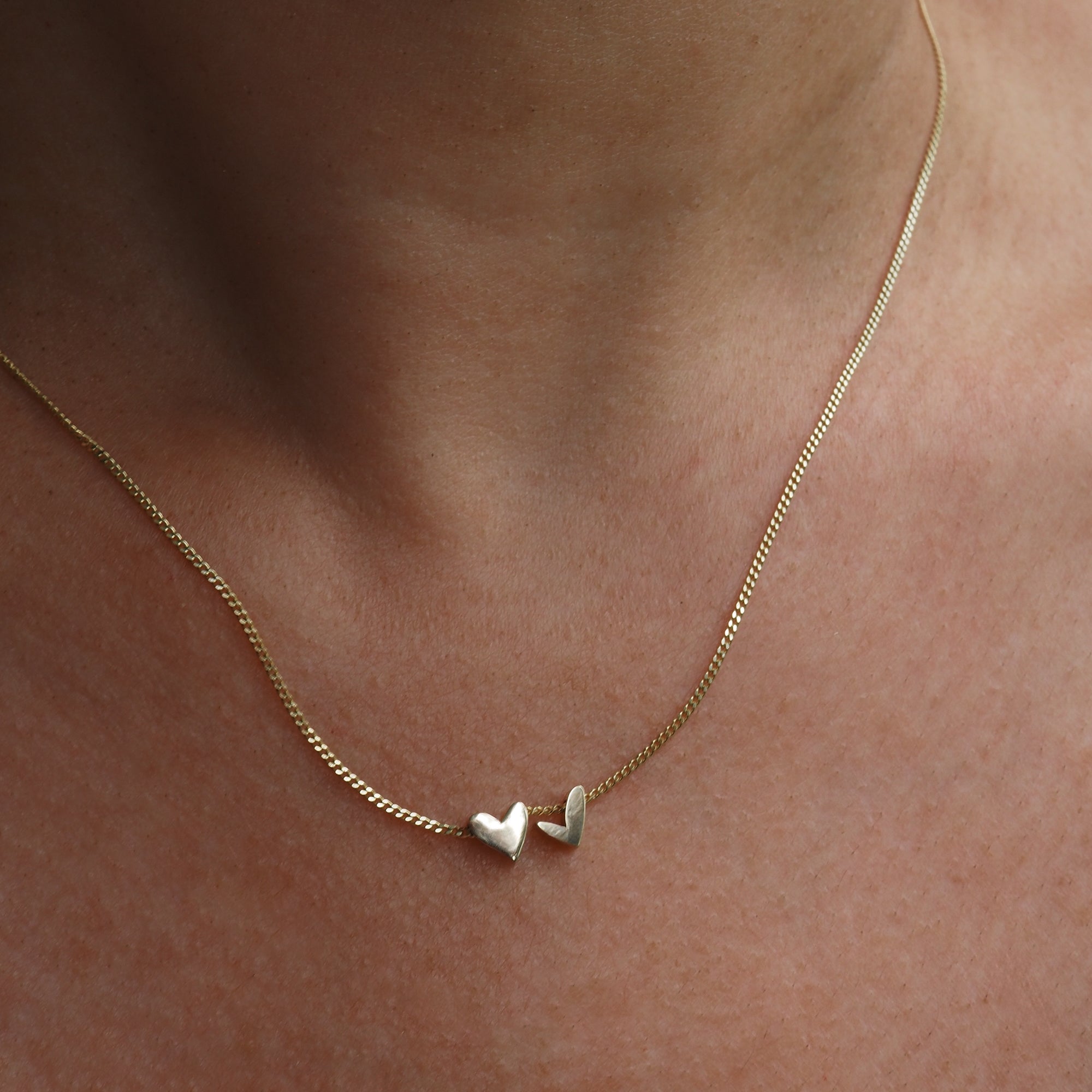 Gold necklace with two small heart pendants elegantly resting on a person's neck, showcasing minimalist luxury jewellery design.