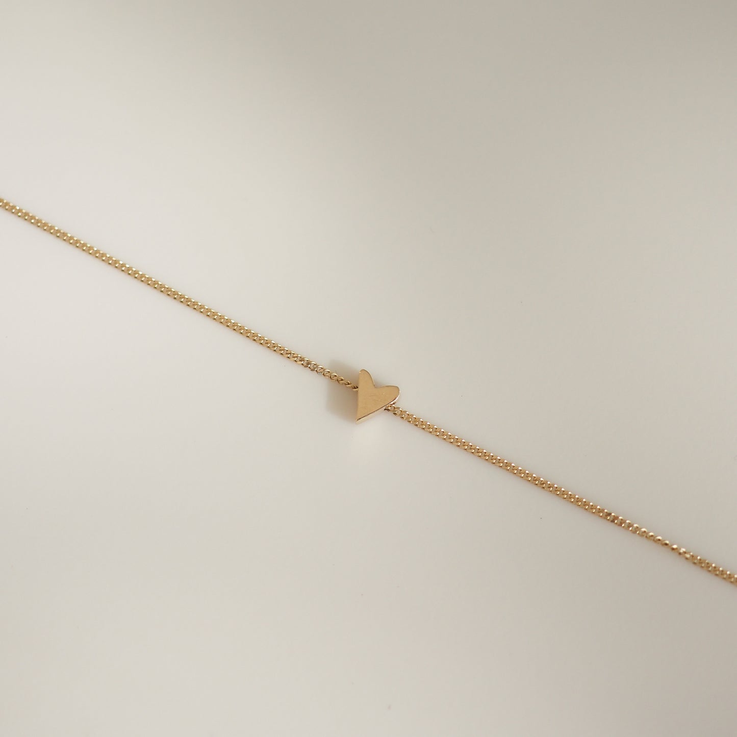 Elegant gold bracelet with a delicate chain and a minimalist heart charm, set against a neutral backdrop. Luxurious jewellery design.