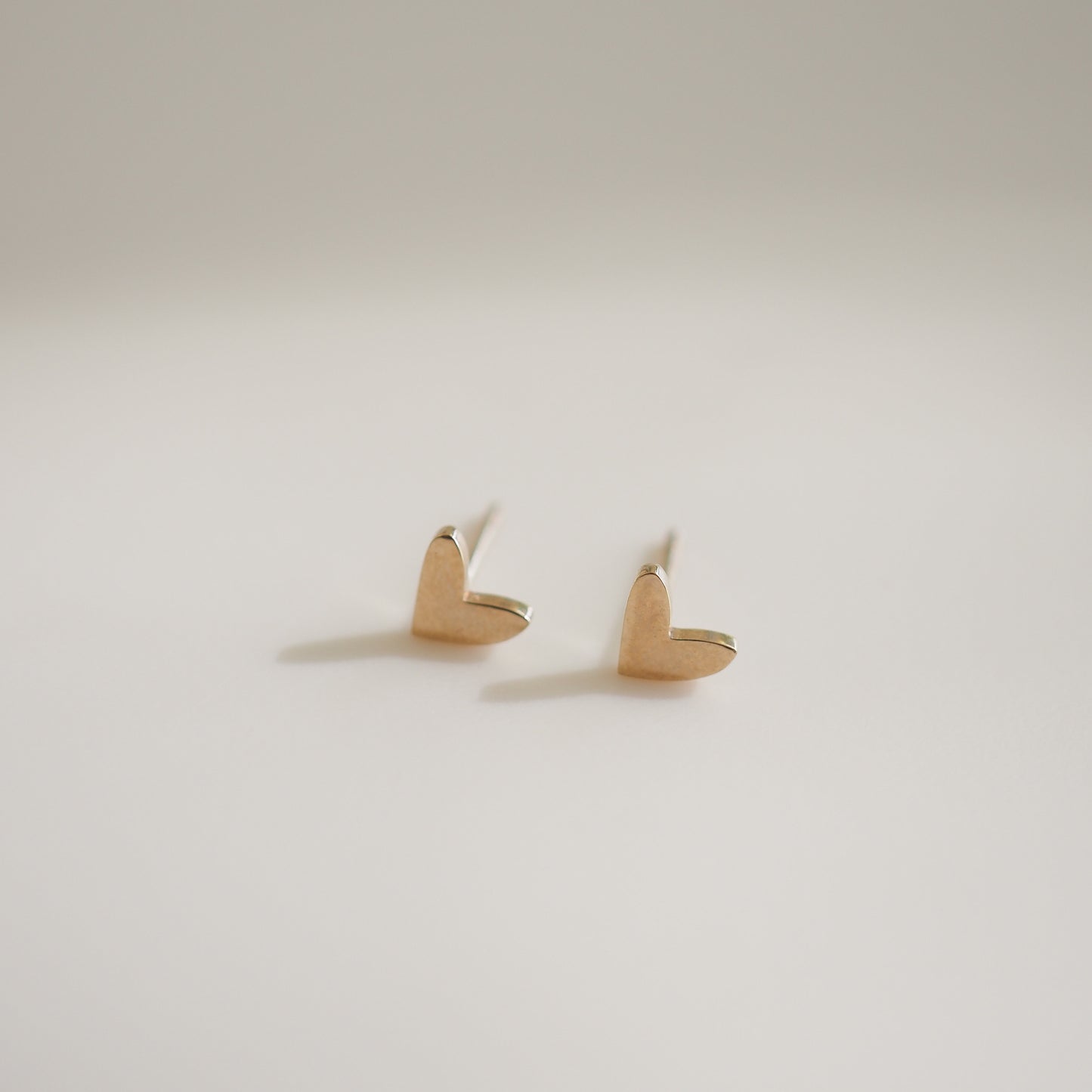 Elegant gold heart stud earrings on a plain background, showcasing minimalist luxury jewellery design.