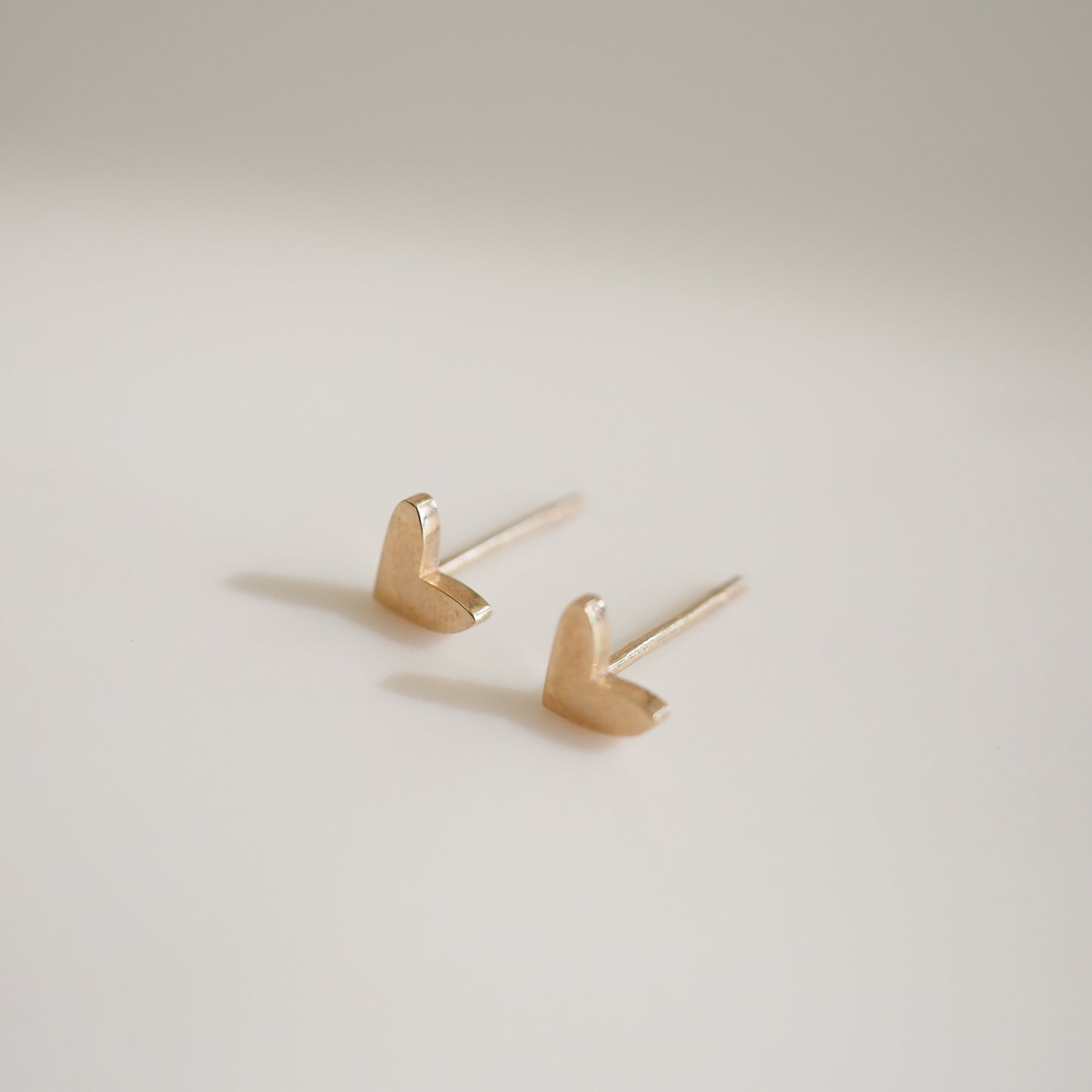 Gold heart-shaped stud earrings displayed on a light background, showcasing elegant minimalist design in luxury jewellery.