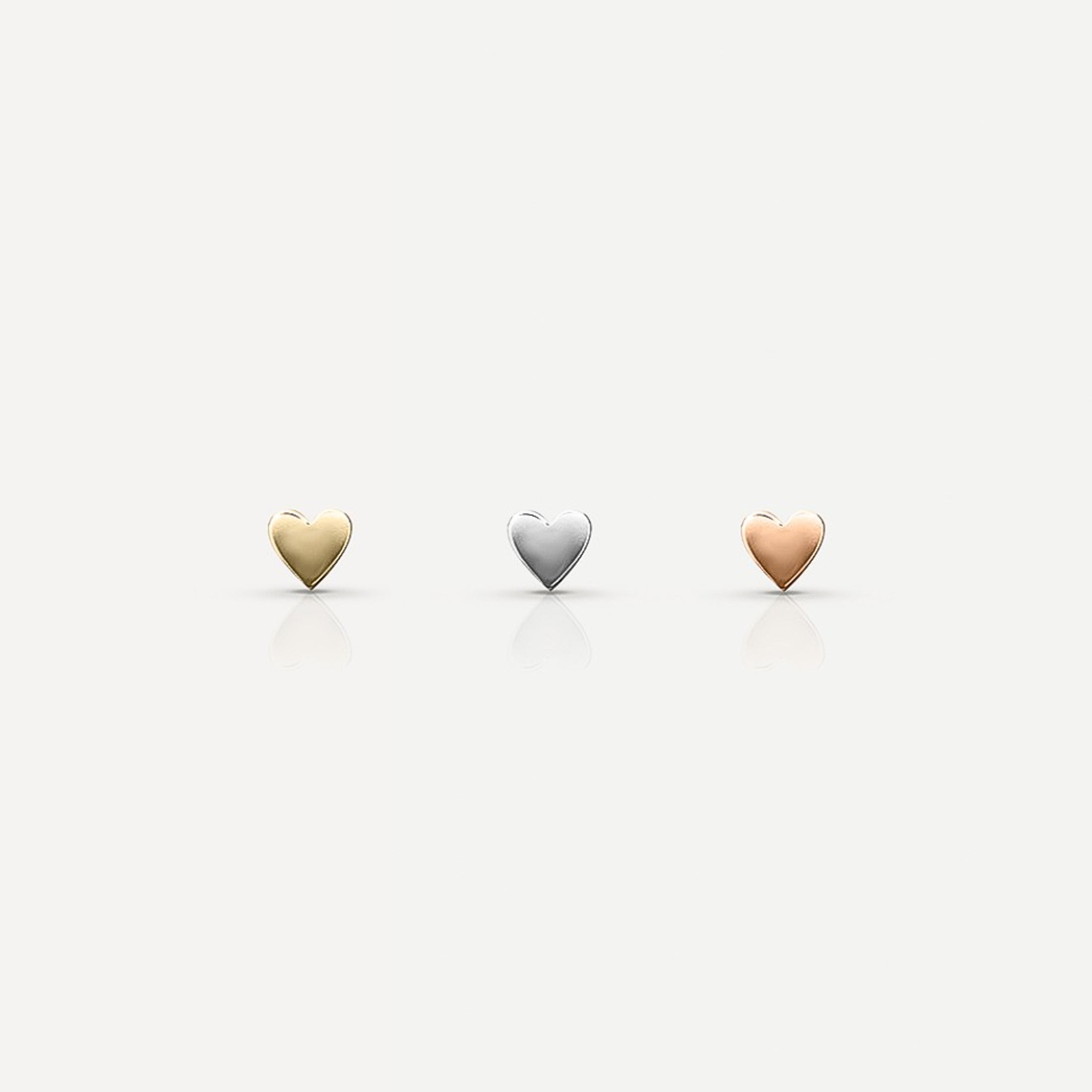 Three heart-shaped jewellery pieces in gold, silver, and rose gold on a plain background, reflecting a luxury aesthetic.