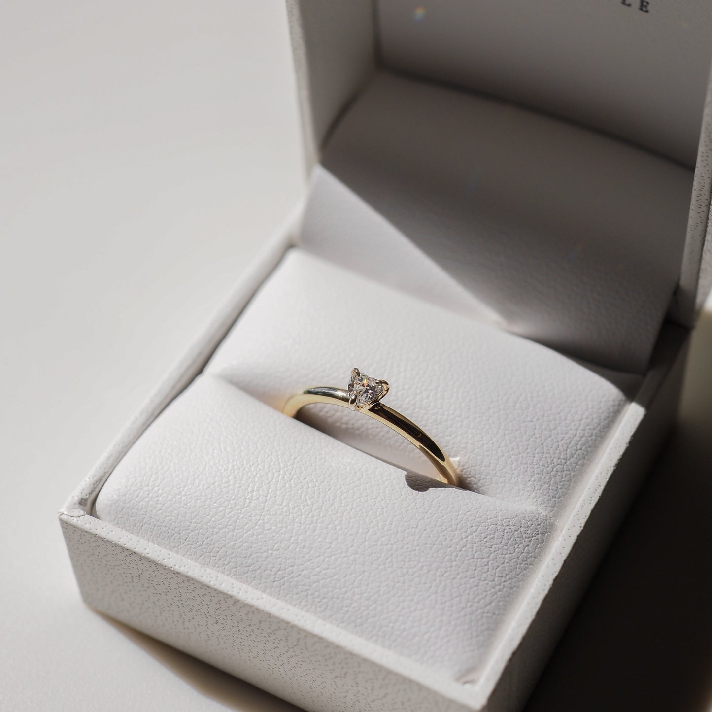 Gold engagement ring with a single diamond stone in an open white leather jewellery box. Sophisticated and elegant design.