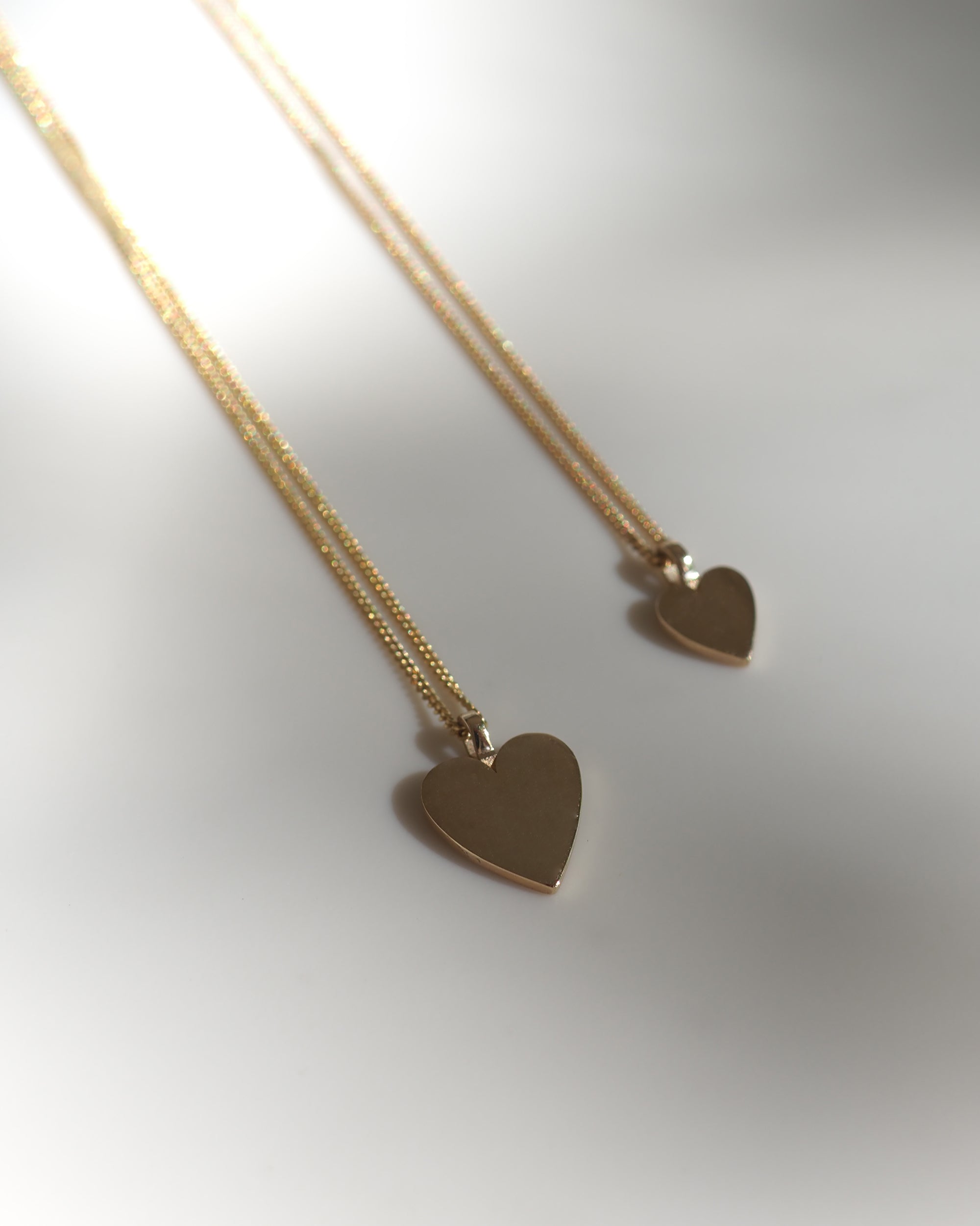 Two gold heart-shaped pendants on delicate chains, elegantly displayed on a soft background. Perfect example of luxury jewellery design.