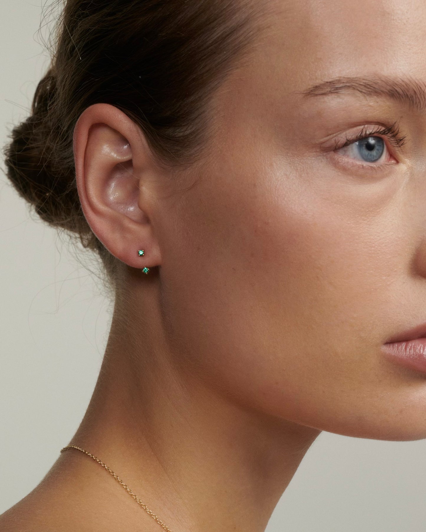 Close-up of a person wearing a green earring with a neutral background