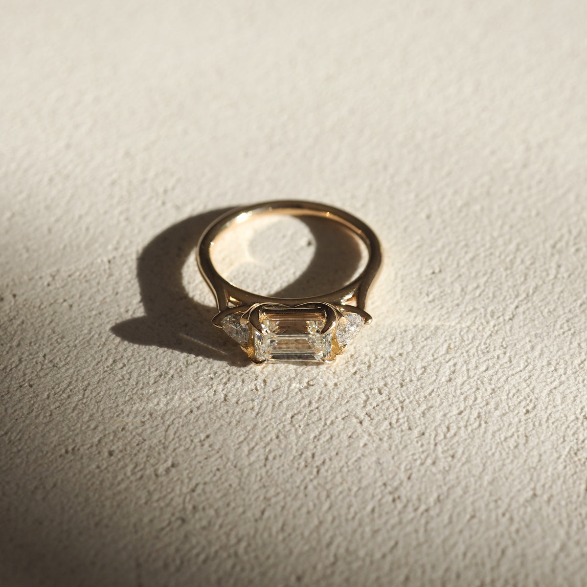 Elegant gold ring with a rectangular emerald-cut diamond, side stones catching light on textured surface. Luxurious jewellery, classic design.