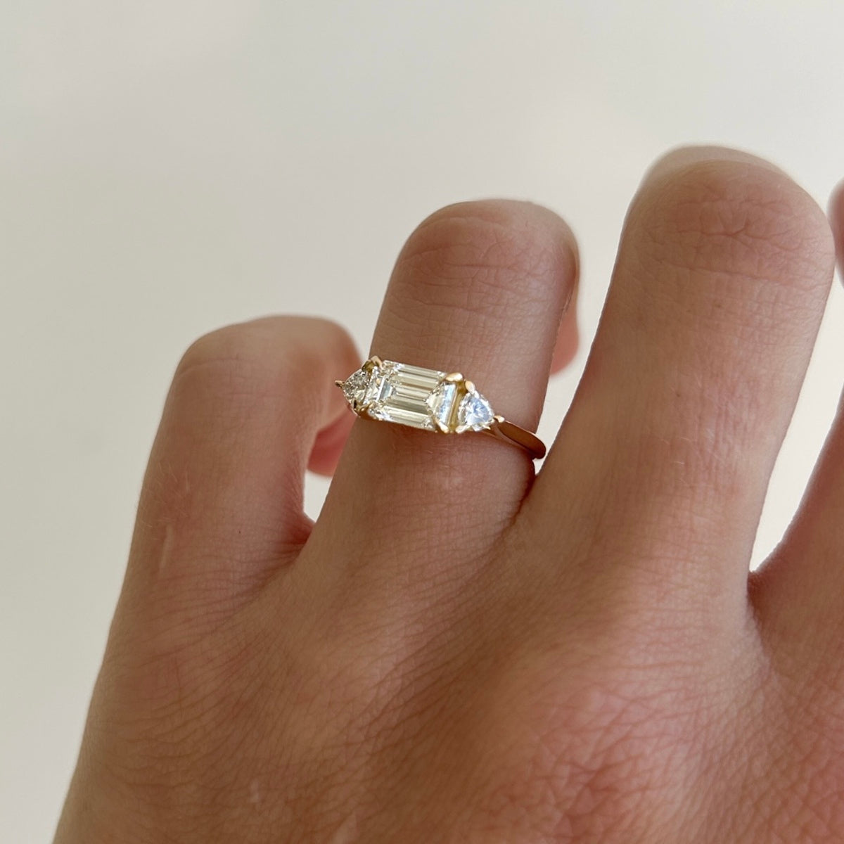 Isla showcases the timeless beauty of a 1.27ct emerald & trillion trilogy lab-grown diamond ring set in solid 18ct yellow gold. 