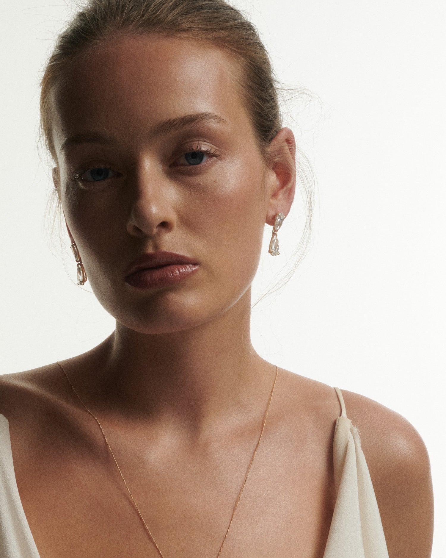 Woman wearing earrings and a necklace against a plain background