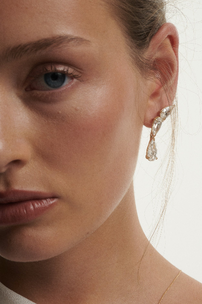 Close-up of a woman wearing a gold earring with a lab grown drop diamond earring on a white background