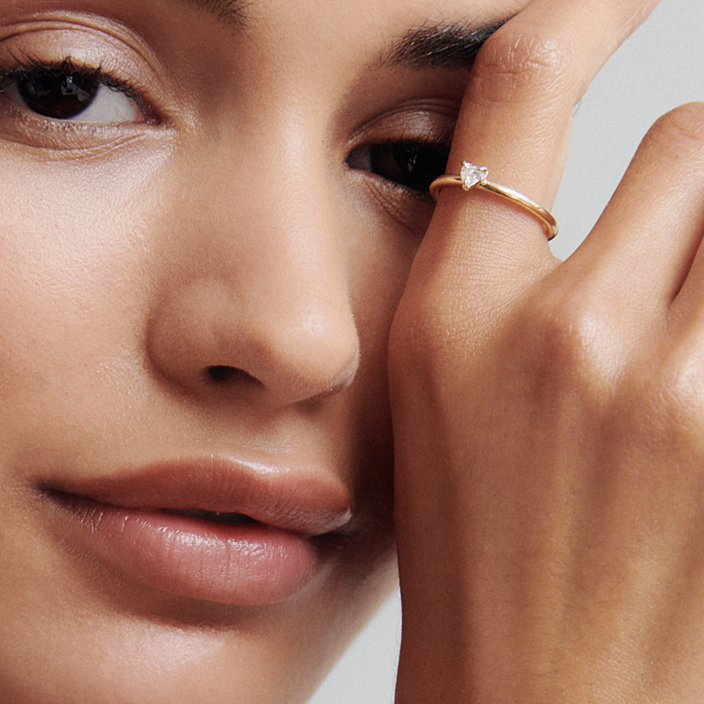 Close-up of a woman wearing a delicate gold ring with a solitaire diamond, highlighting luxury jewellery. Her hand touches her face gently.