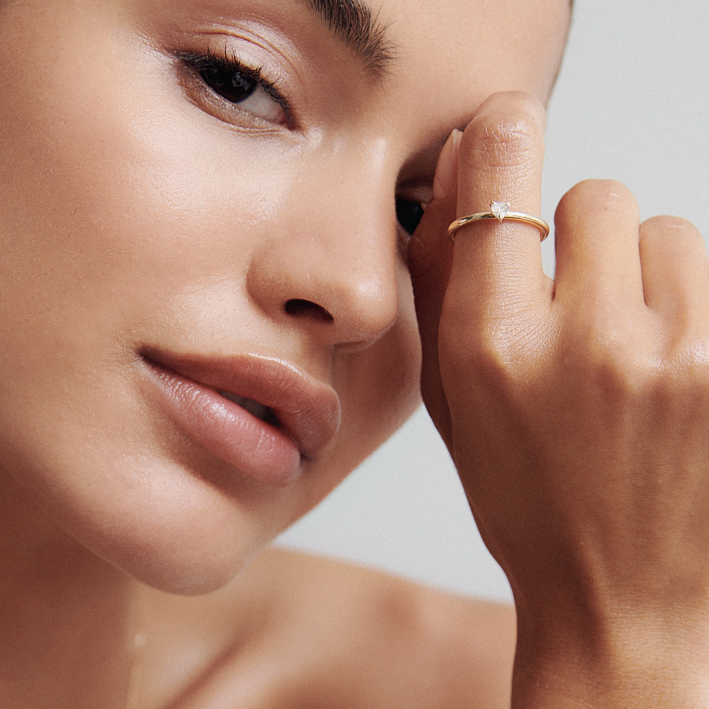 Close-up of a woman wearing a minimalist gold ring with a solitaire diamond, highlighting luxury jewellery against her clear skin.